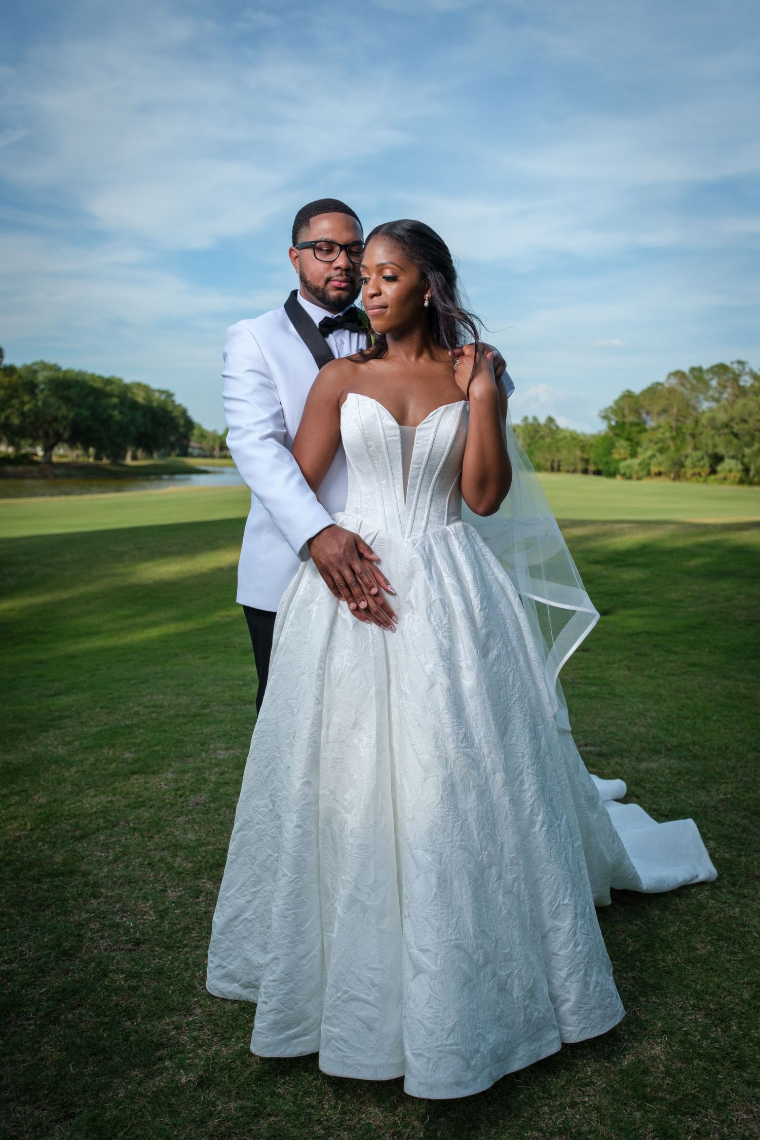 Elegant bride and groom posing on a lush golf course, wearing white wedding gown and white tuxedo jacket.