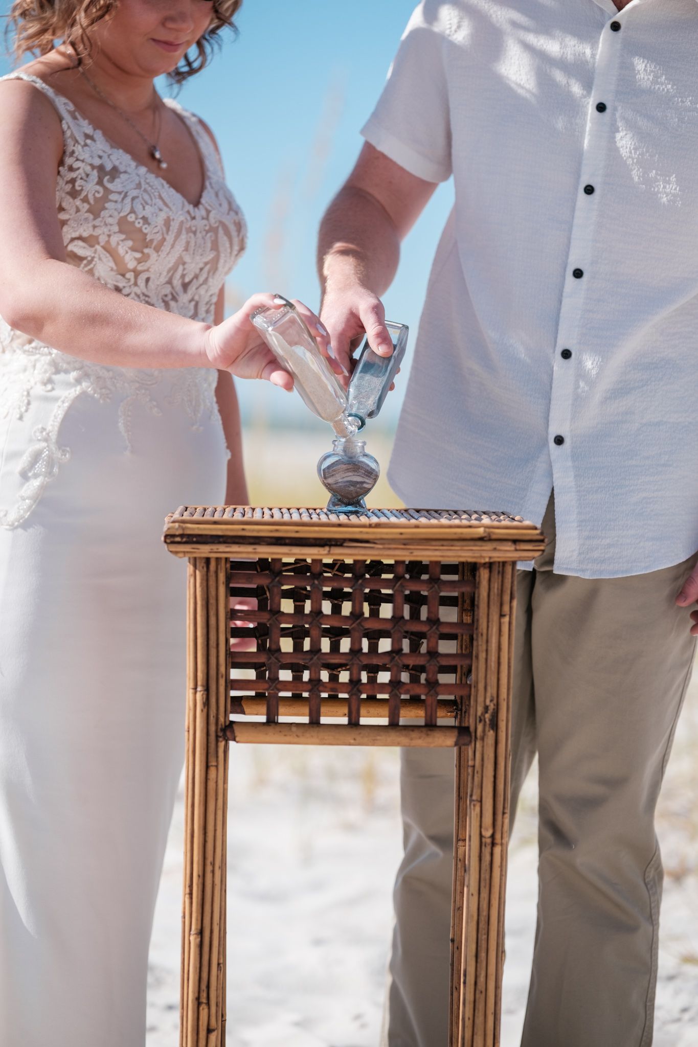 Wedding ceremony sand unity ritual performed at wooden table on beach.