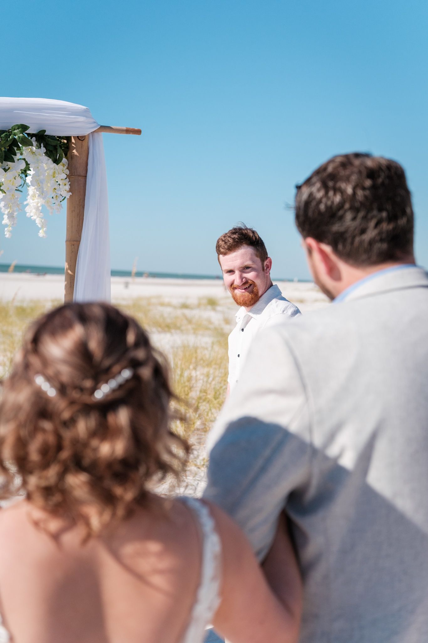 A beach wedding ceremony setup with white chairs and an arch against a bright blue ocean backdrop.