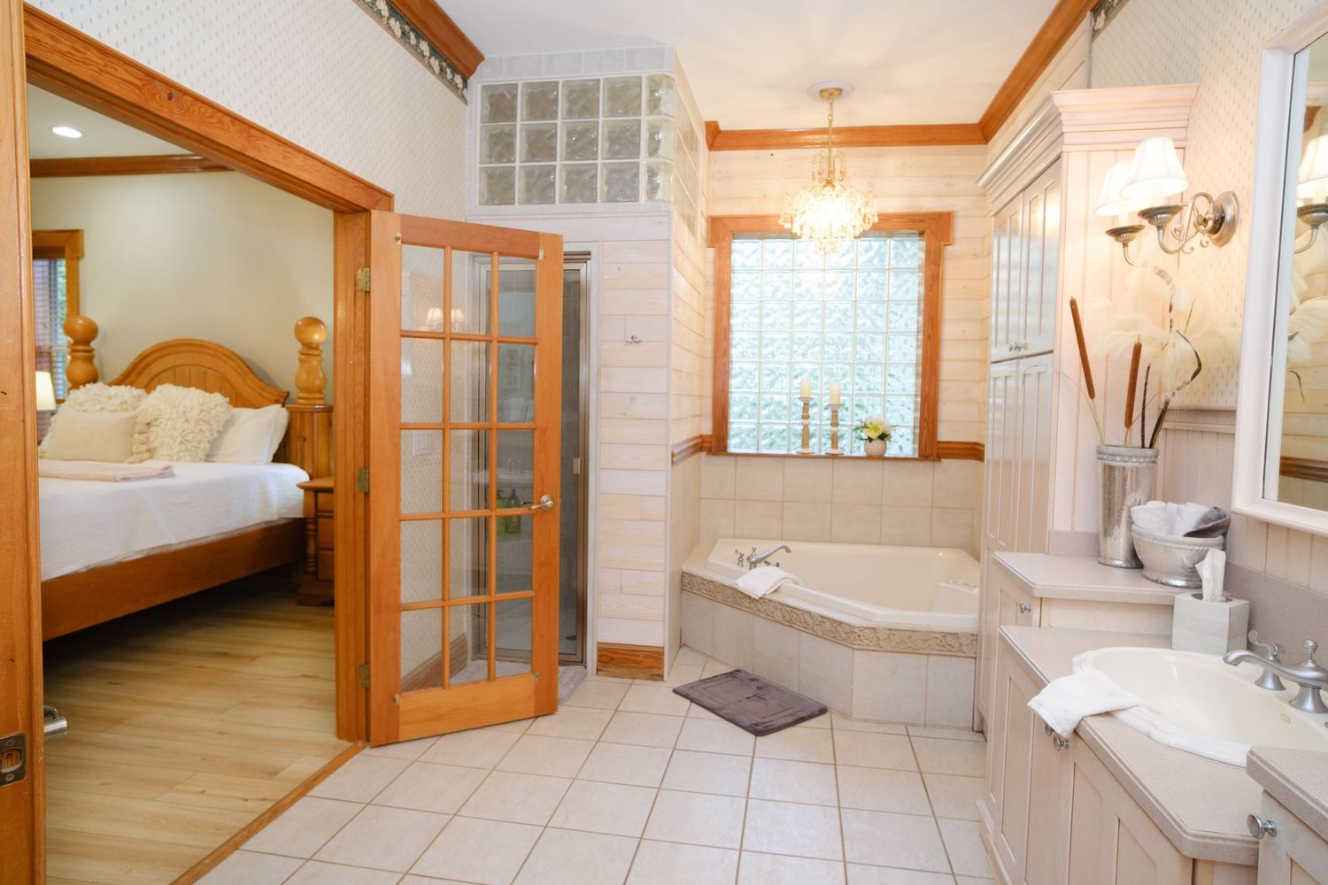Luxury bathroom with corner whirlpool tub, French doors, and wooden trim connected to a bright bedroom suite.