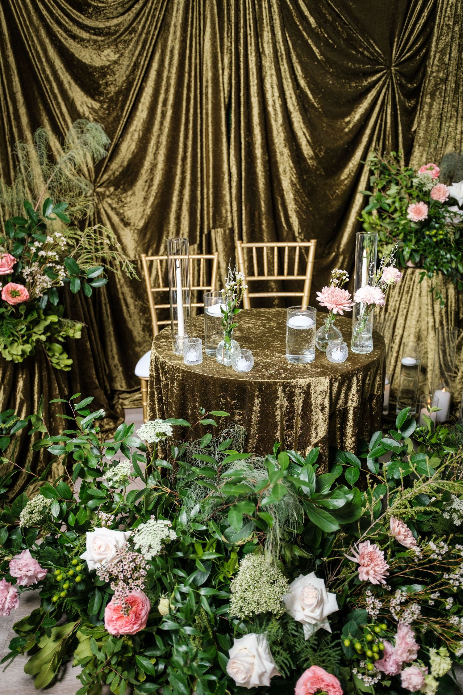 Wedding backdrop with luxurious gold draping, white chairs, and lush floral arrangements in pink and white.