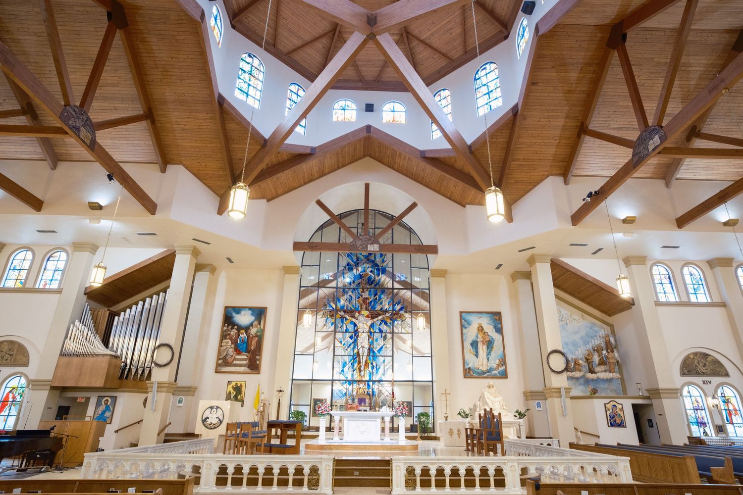 Stunning Catholic church interior with vaulted wood ceiling, blue stained glass cross, and ornate altar in a bright sanctuary.