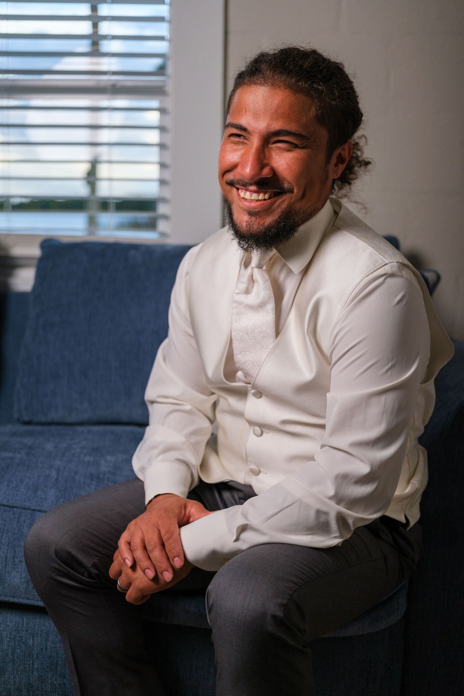 A person in a white button-down shirt sits casually on a navy blue couch in an office setting with natural lighting.