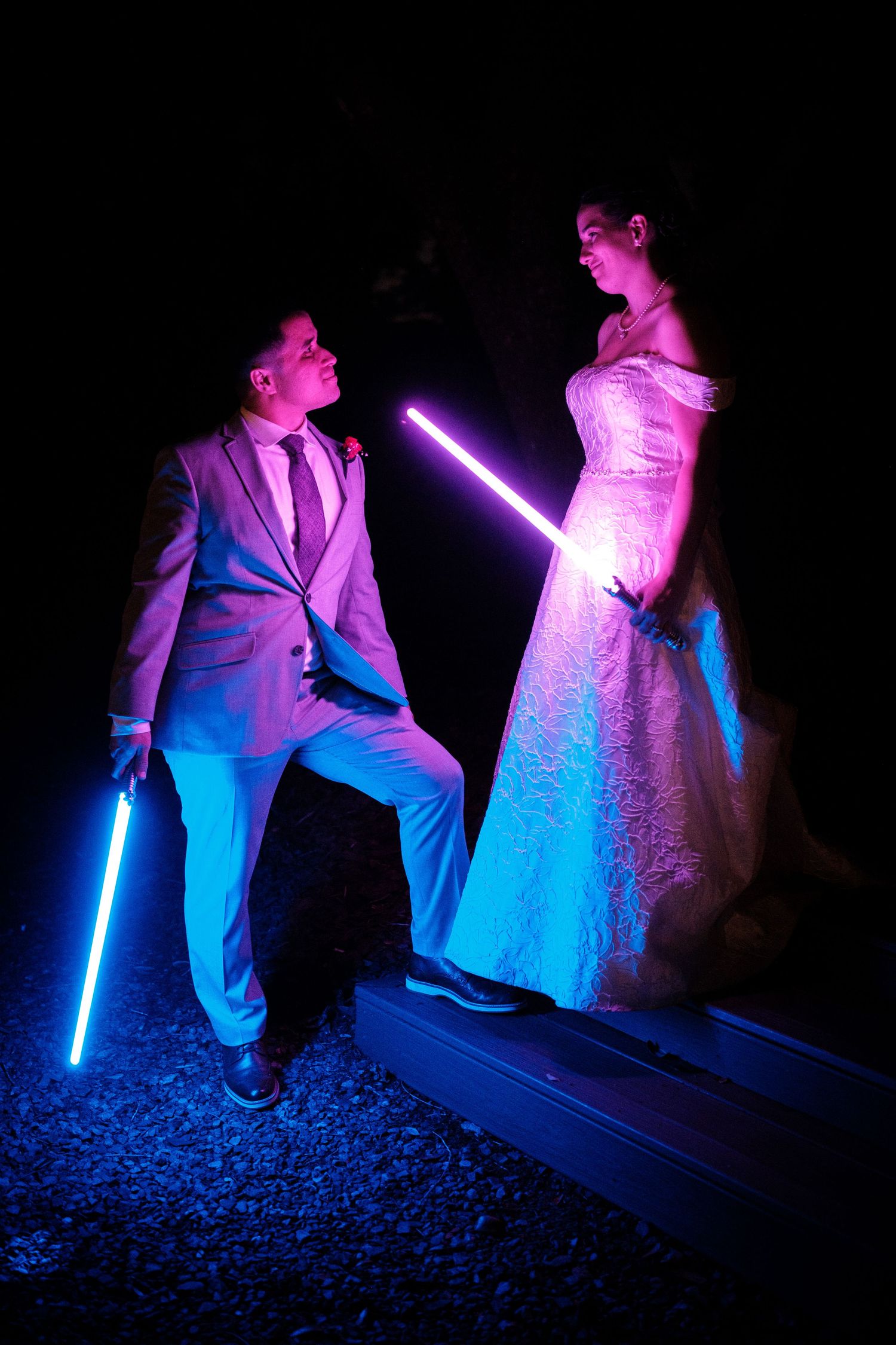 Bride and groom in wedding attire holding glowing lightsabers in a dramatic Star Wars themed photo.