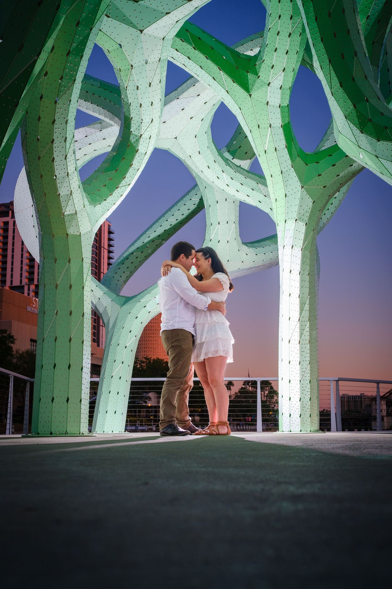 Two people share a romantic moment in downtown Tampa under The Form of Wander Scuplture during their engagement photo session