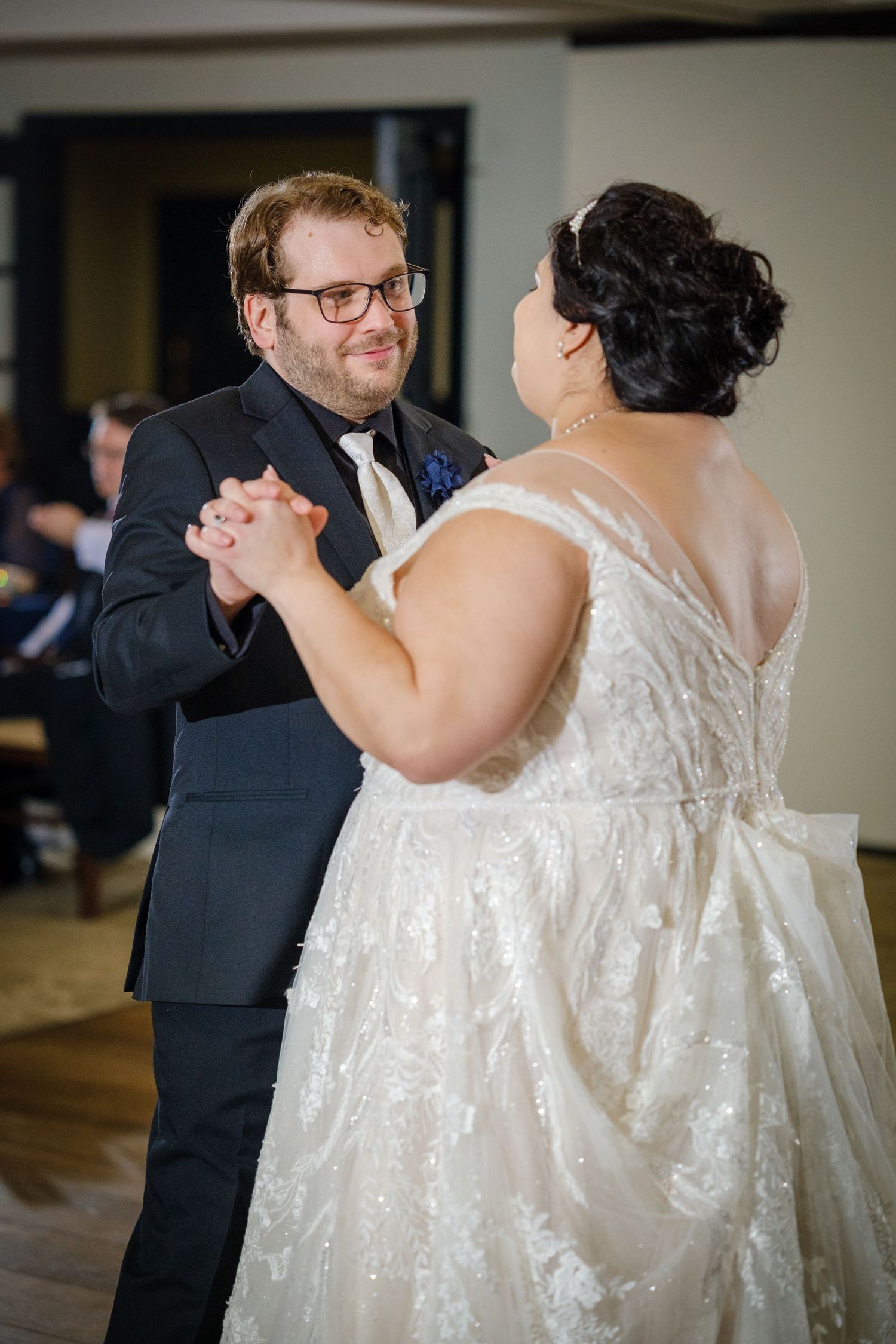 A couple shares their first dance at a wedding reception, with the bride wearing a sparkly white dress.