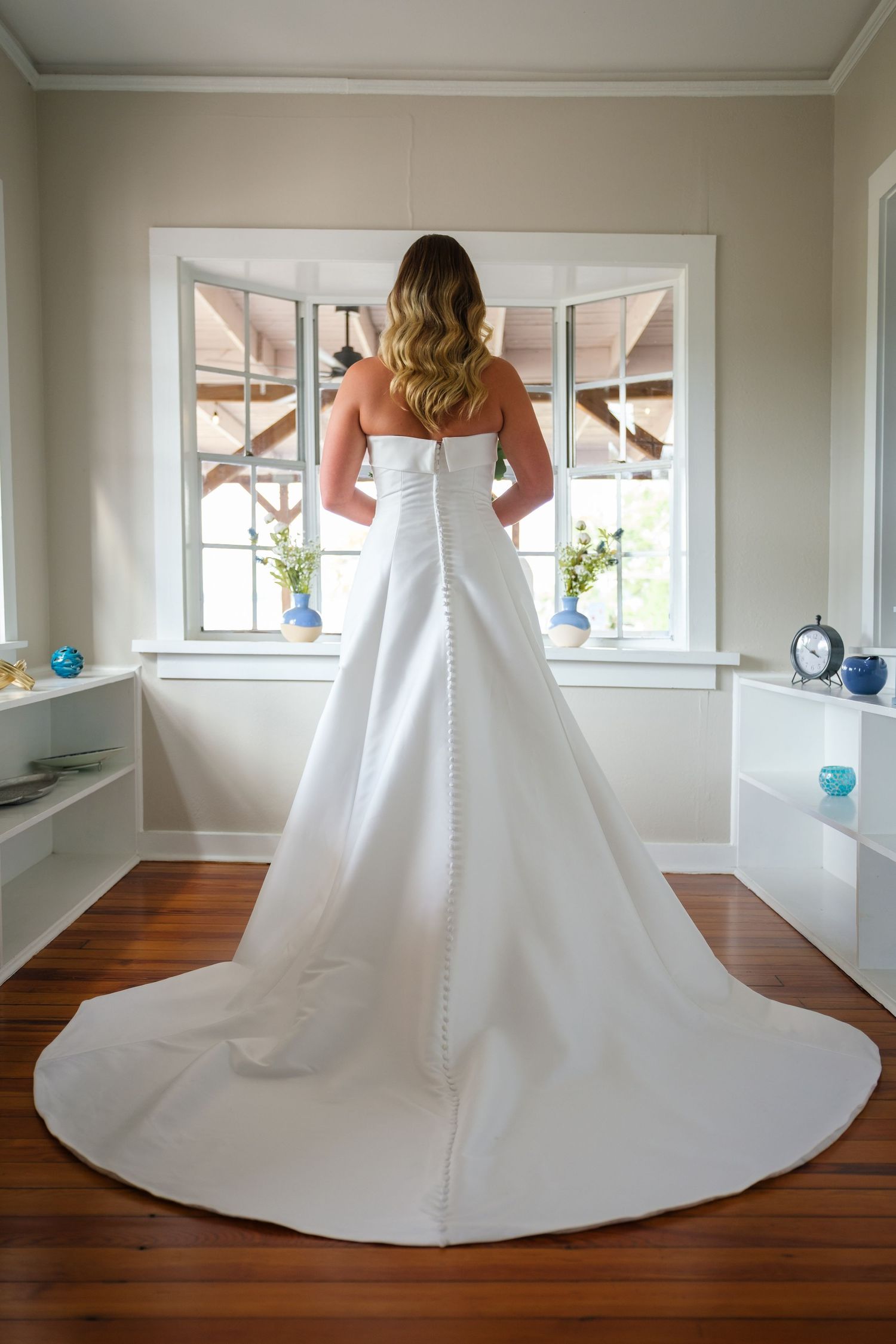 Elegant white wedding dress with dramatic cathedral train displayed on hardwood floor in natural light.