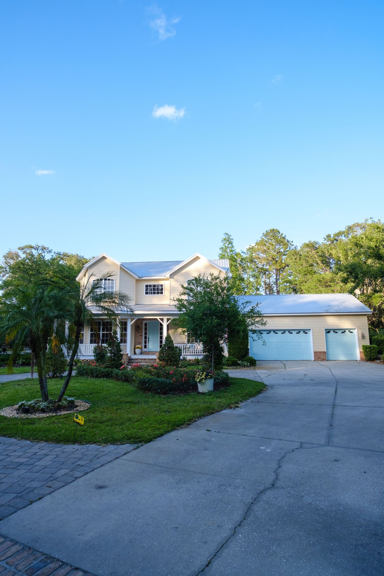 Modern two-story suburban home with white exterior, three-car garage and circular driveway surrounded by palm trees.
