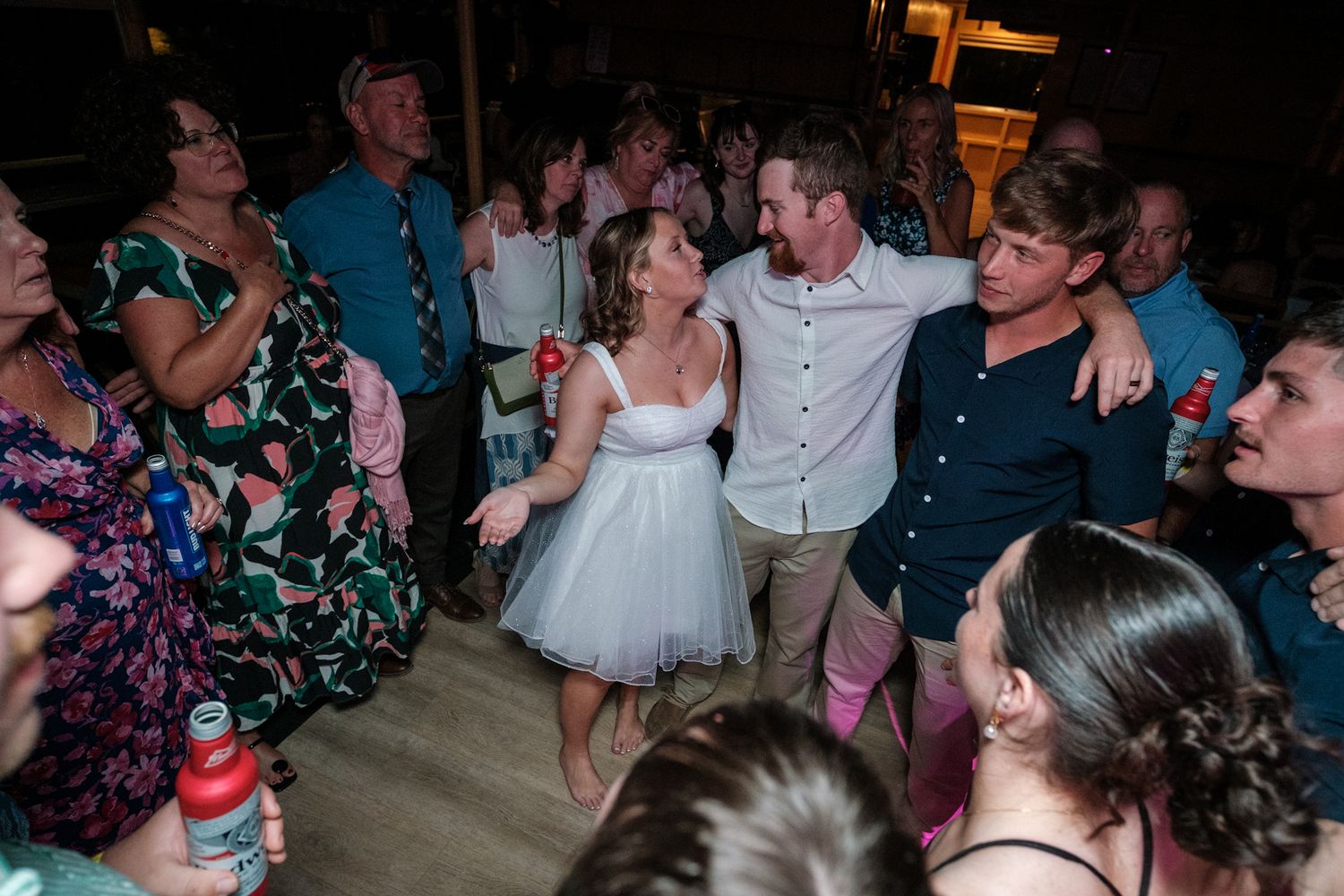 Wedding guests dancing and celebrating together on a dimly lit dance floor during the reception.