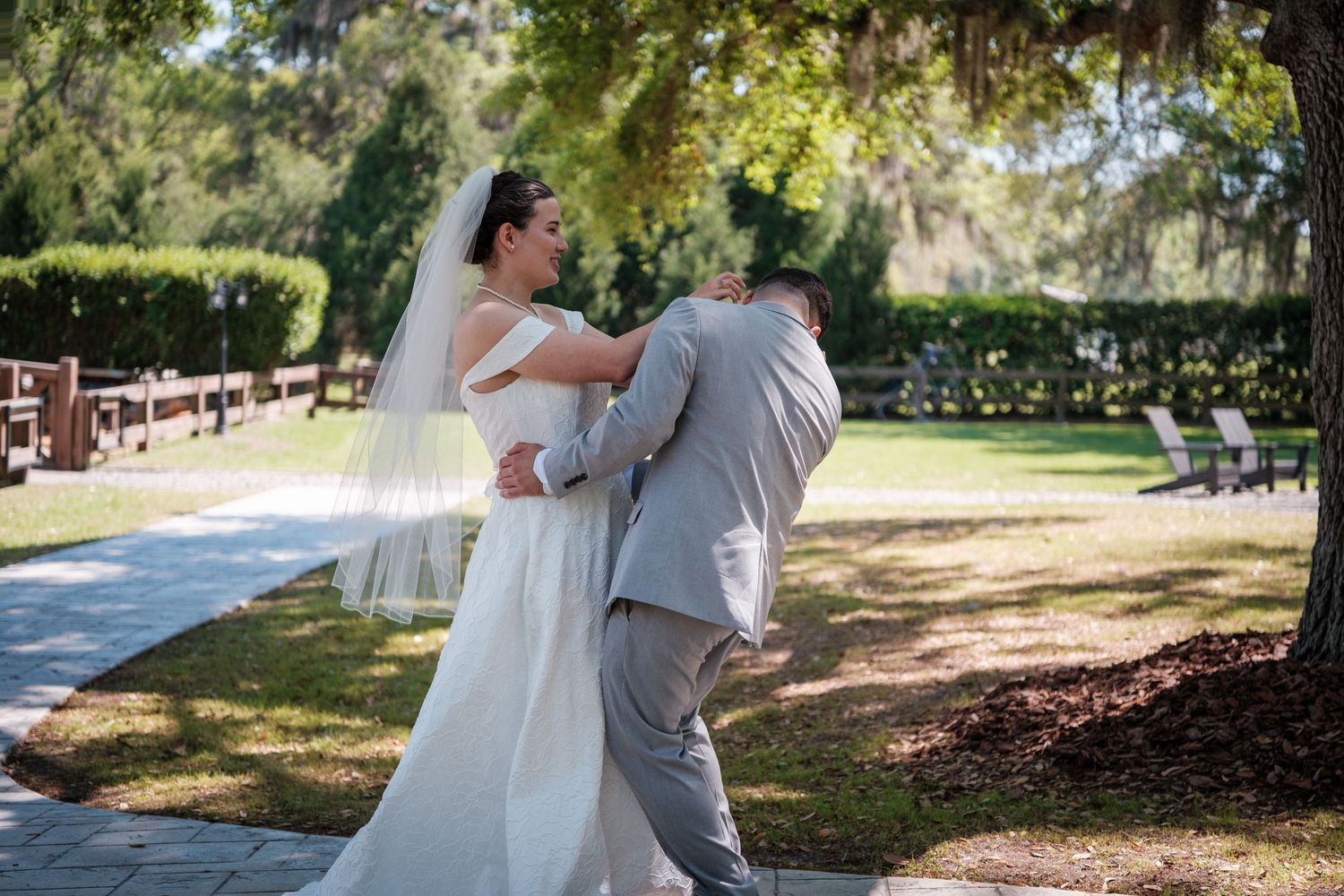 Bride and groom share an emotional first look moment outdoors, surrounded by lush green trees at a sunny wedding venue.