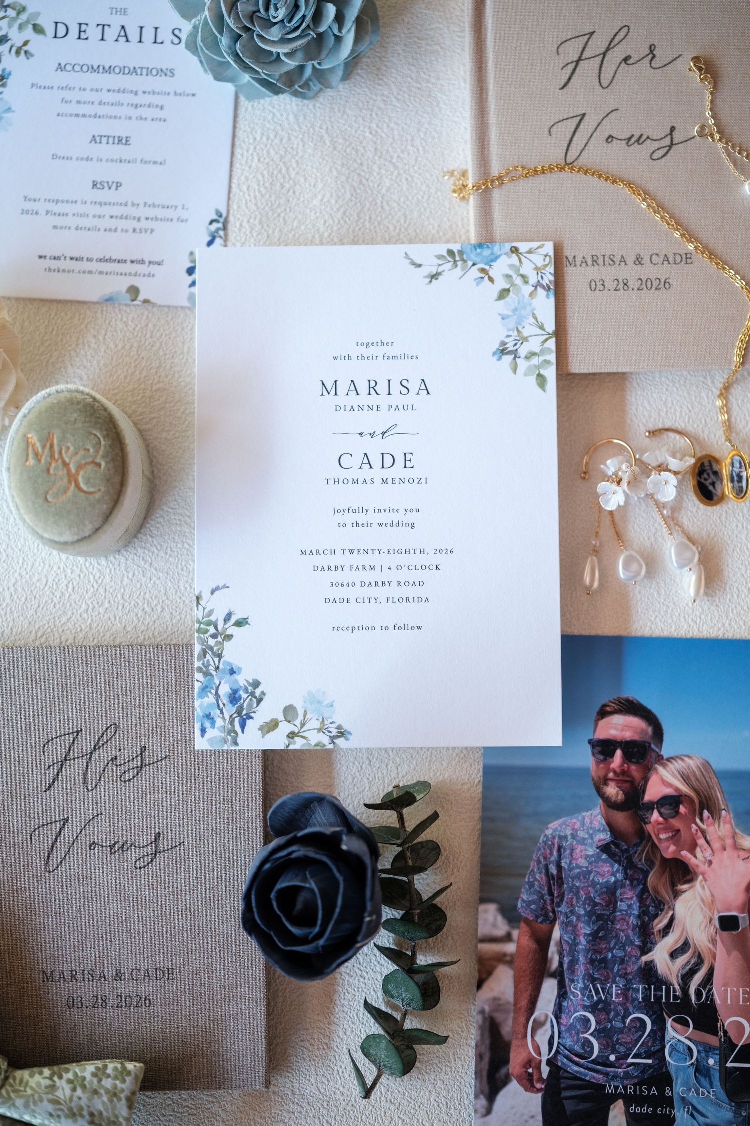 Wedding invitation suite for Marisa and Cade featuring blue floral details, vow books, save the date cards, and elegant gold jewelry.
