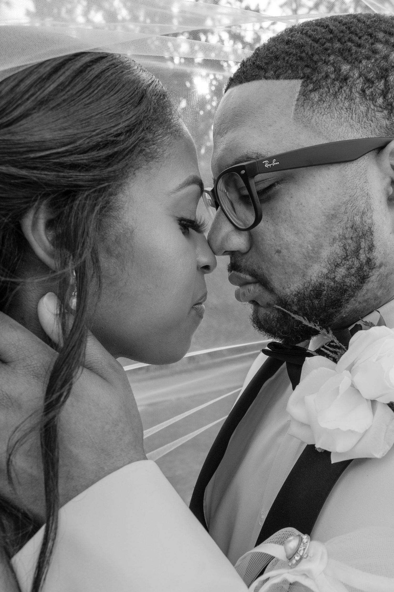 Black and white photo of a couple in wedding attire sharing a romantic kiss, bride in veil and groom in bow tie.