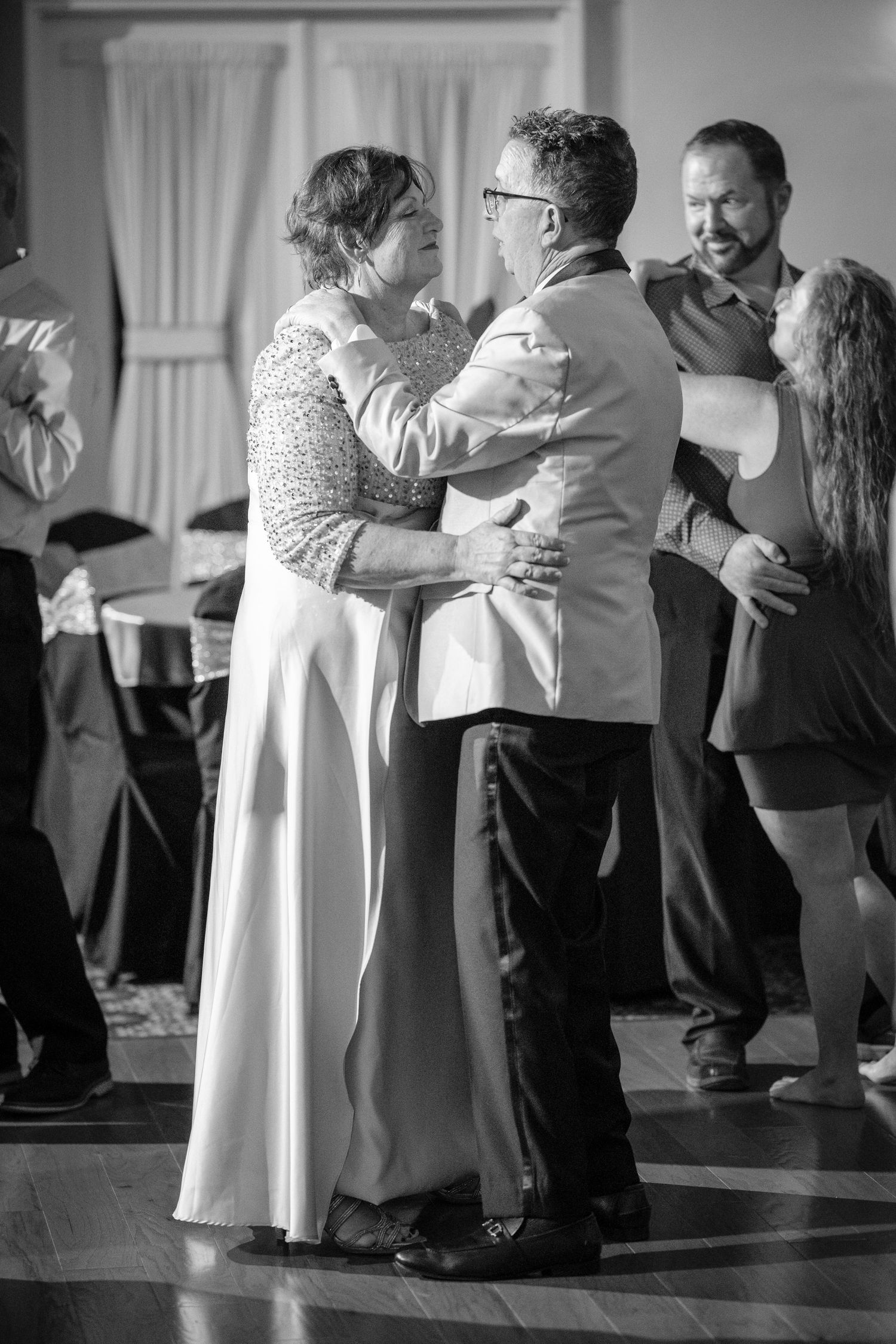 A couple dances together at a formal event while other guests look on in this black and white photograph.