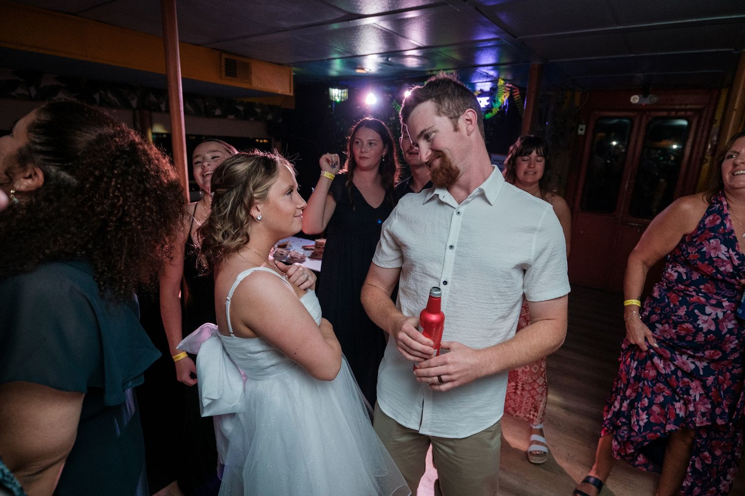 A couple dances together at a wedding reception party with colorful lighting in the background.