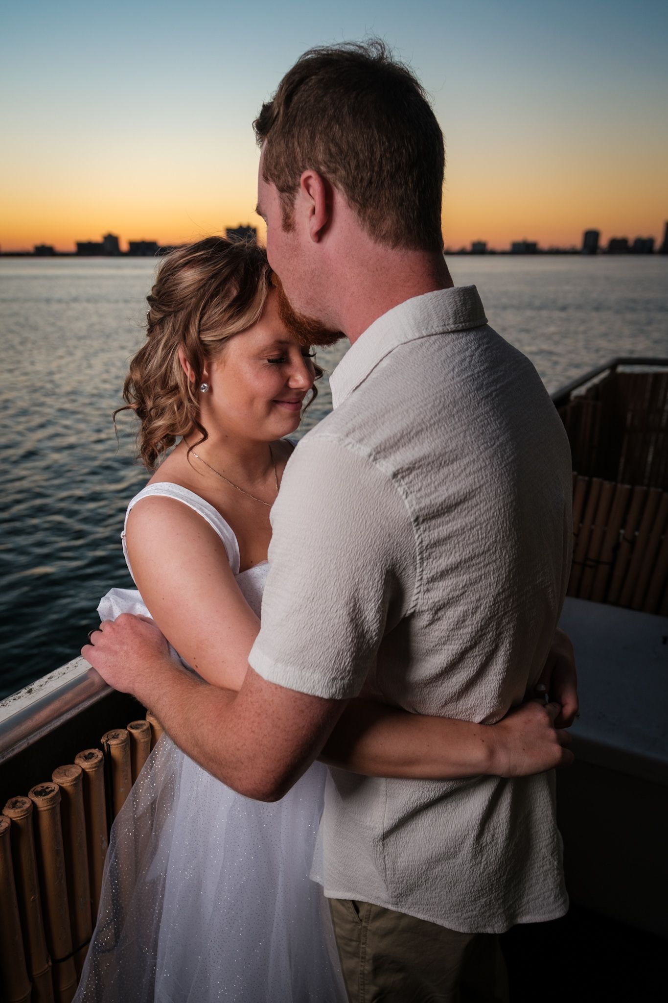 Romantic sunset photos of newlyweds embracing by waterfront with golden hour lighting.