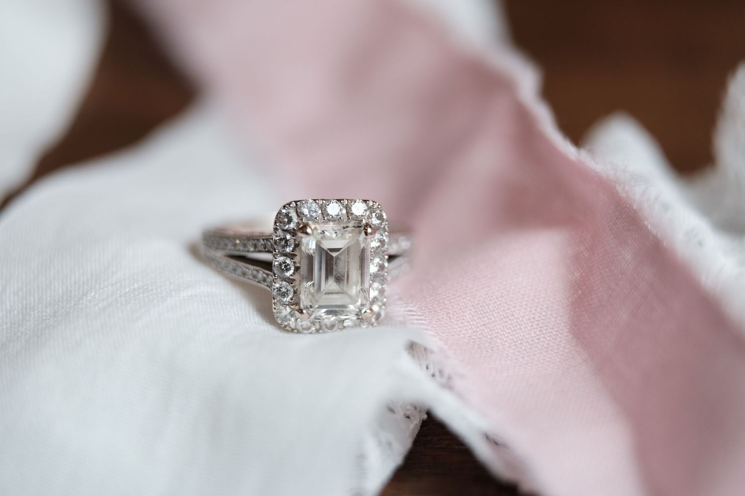 Close-up view of a sparkling diamond engagement ring on pink satin fabric.