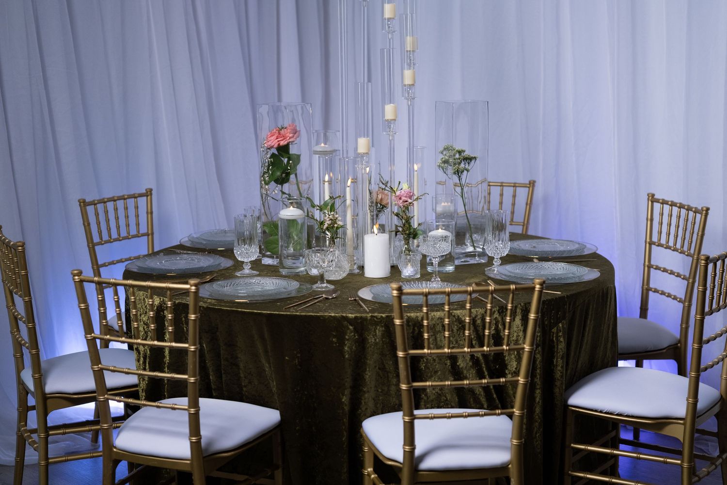 Formal table setting with gold chiavari chairs, black tablecloth, and tall glass candle holders.