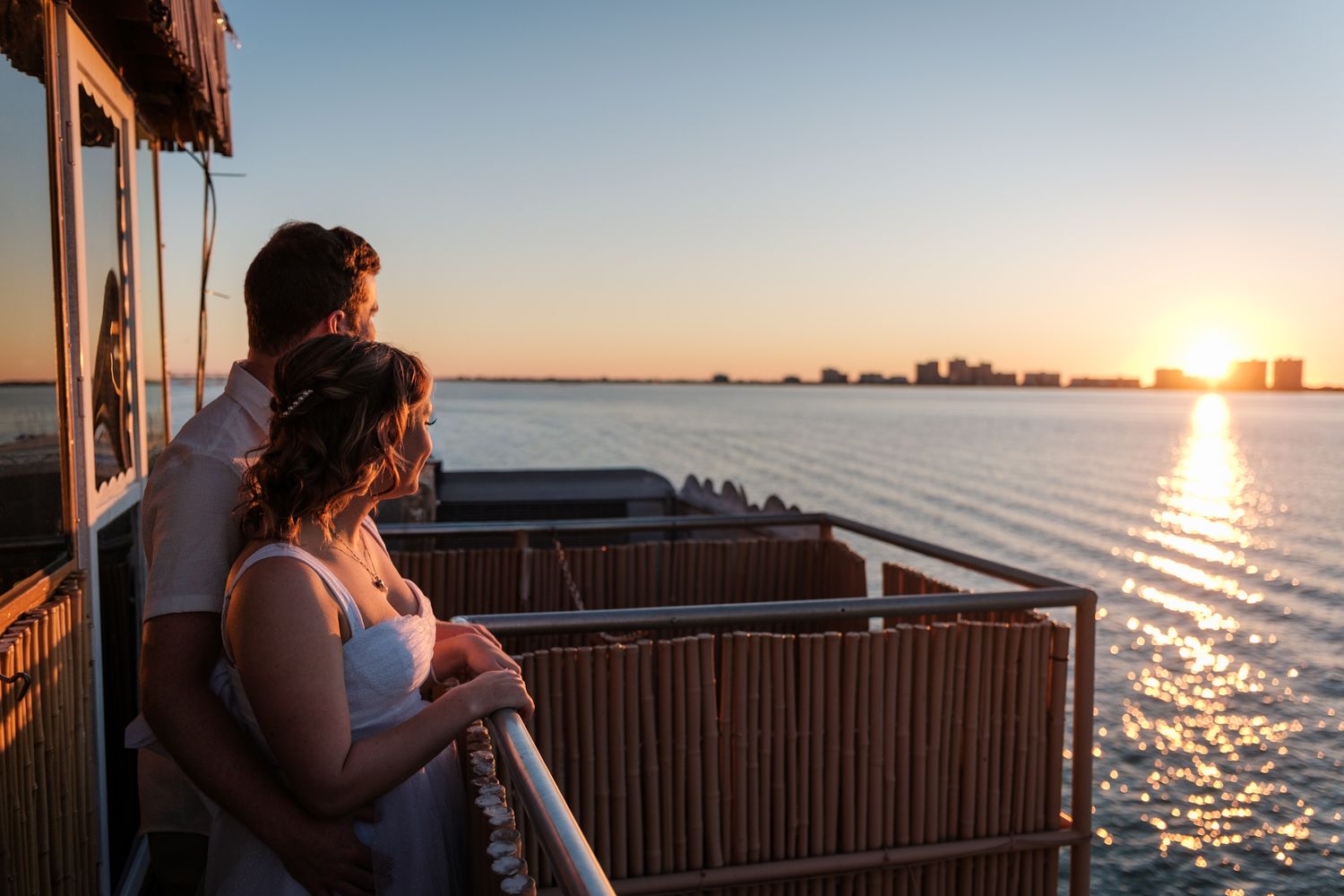 Sunset view over water with silhouetted railings and buildings creating a peaceful waterfront scene.
