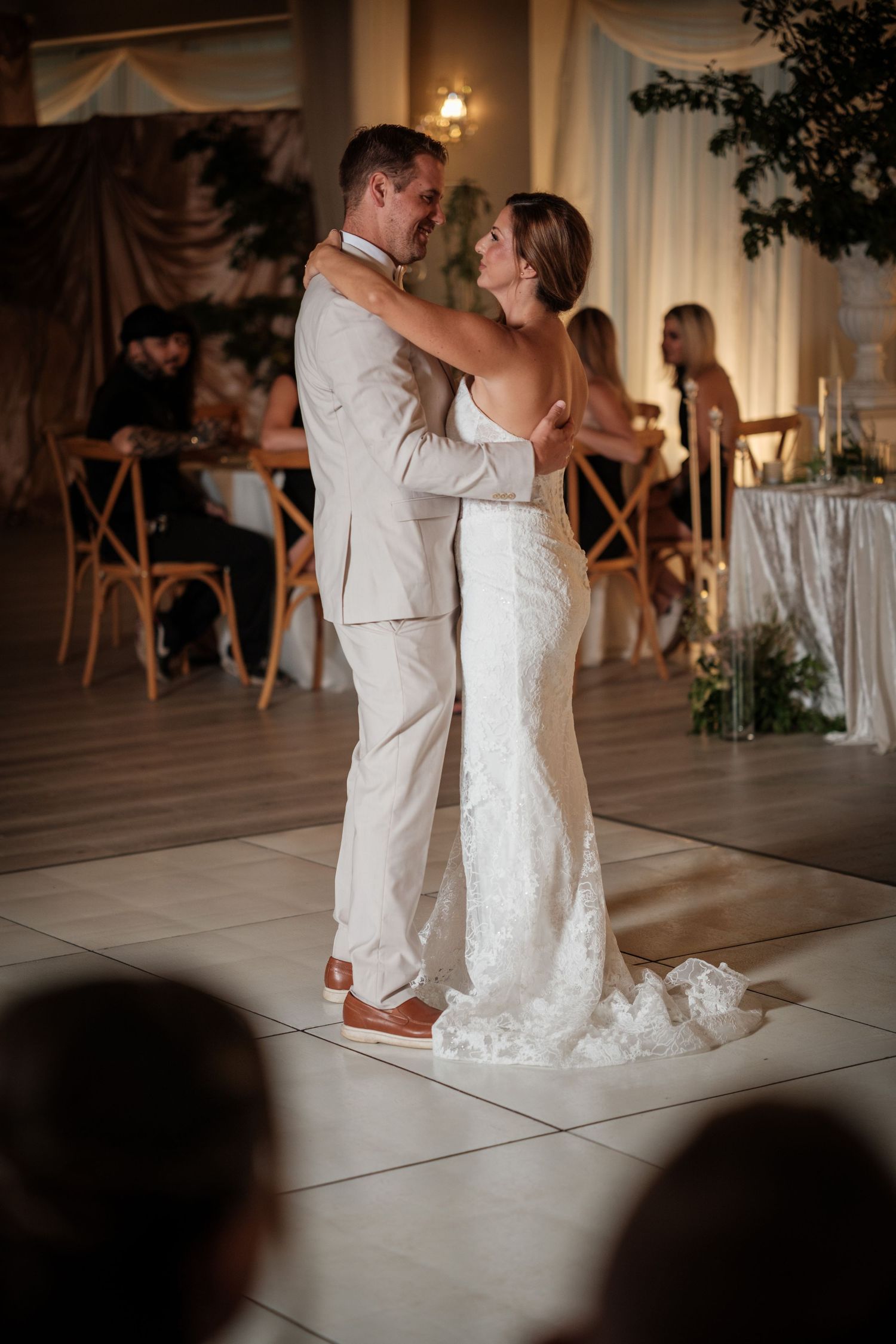 Bride and groom share their first dance on a white dance floor at an elegant wedding reception.