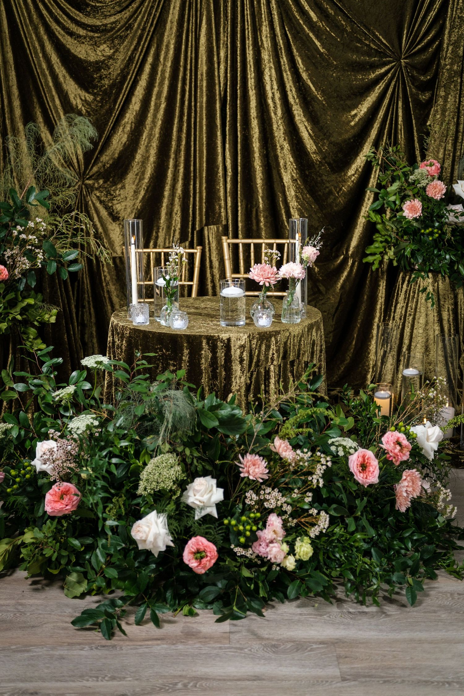 Elegant wedding decor featuring gold draped curtains with pink and white roses and greenery arrangements.