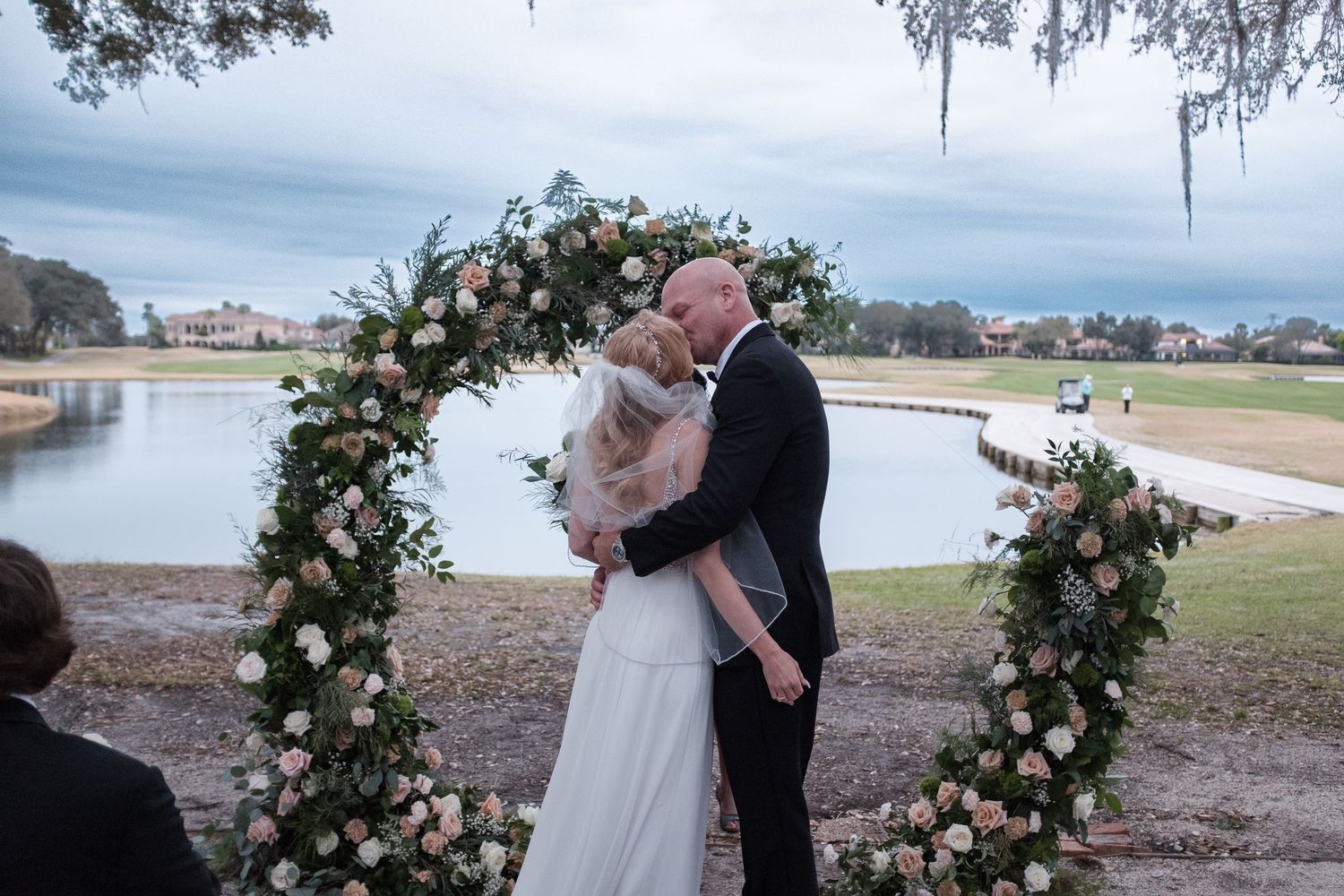 A romantic outdoor wedding scene with floral arches and Spanish moss draped trees in the background.