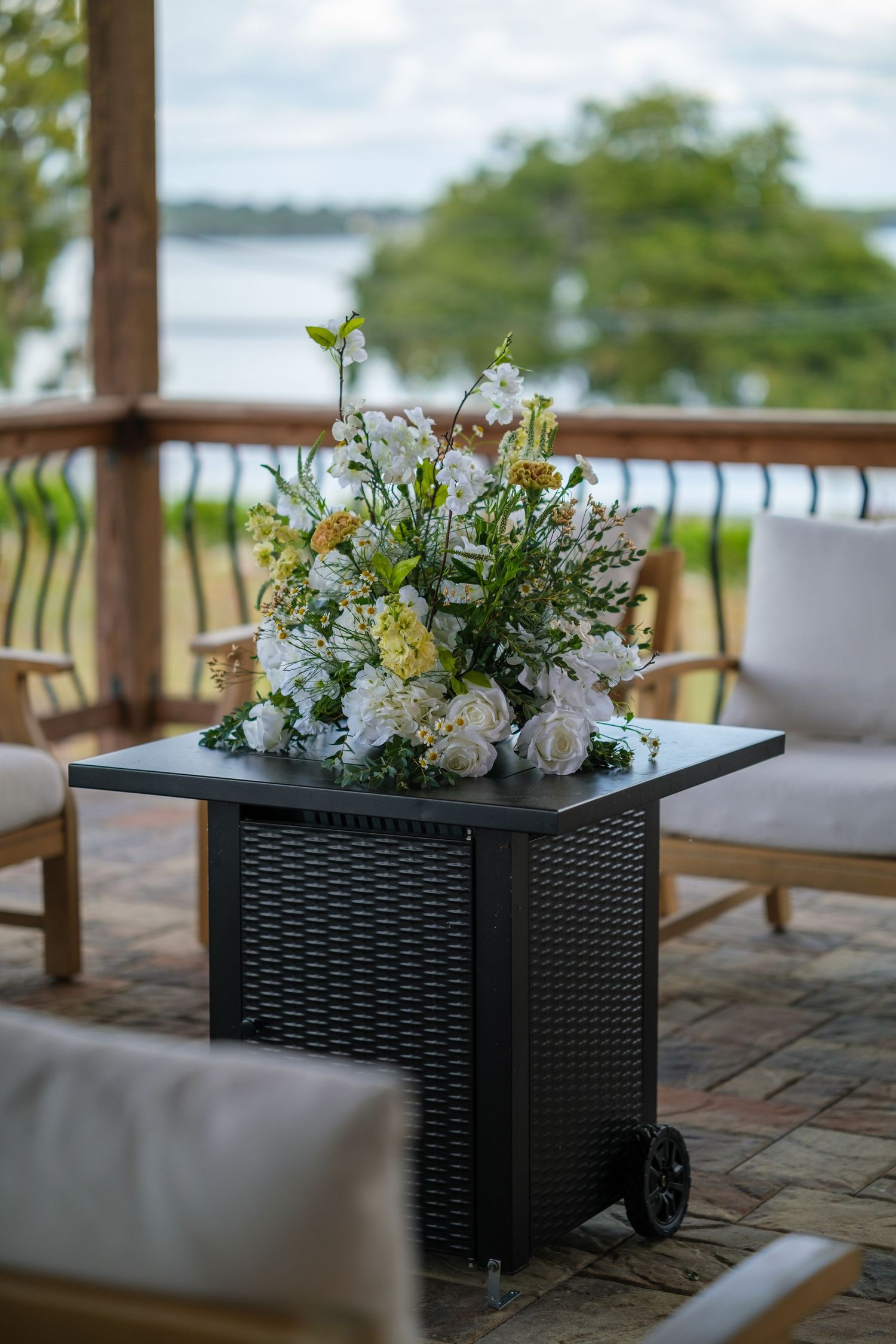 Black wicker planter boxes filled with white floral arrangements on outdoor patio overlooking water.