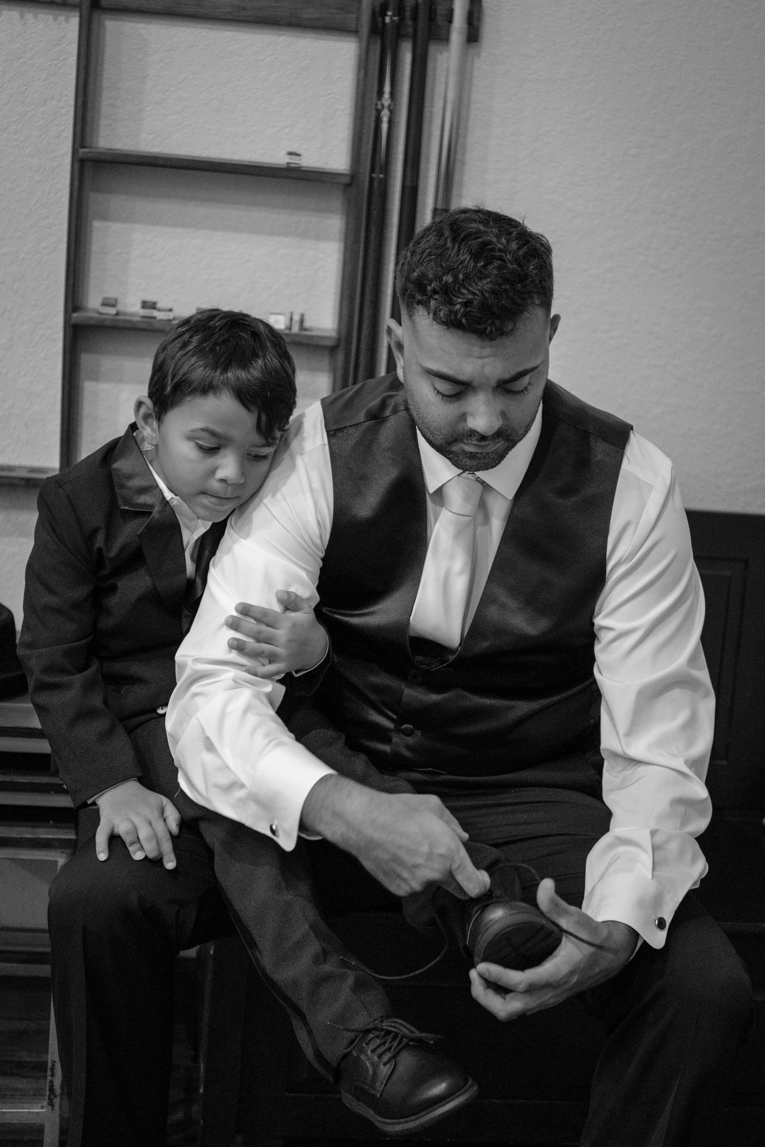 Black and white image showing formal attire preparation with focus on dress shoes and clothing details.