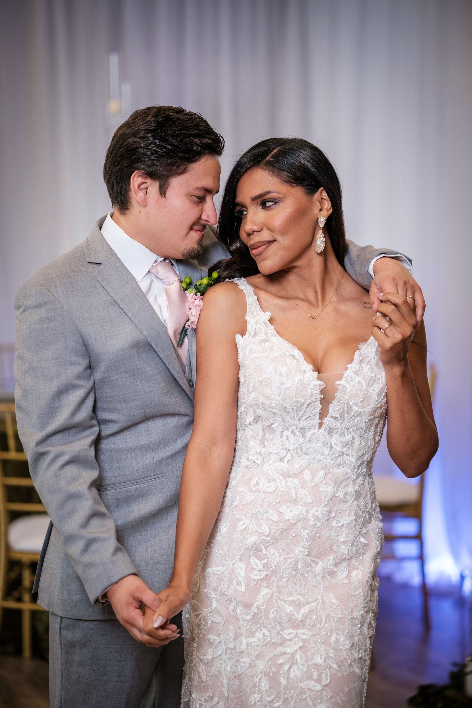 A romantic wedding portrait of a couple in formal attire, with the bride in a lace gown and groom in a gray suit.