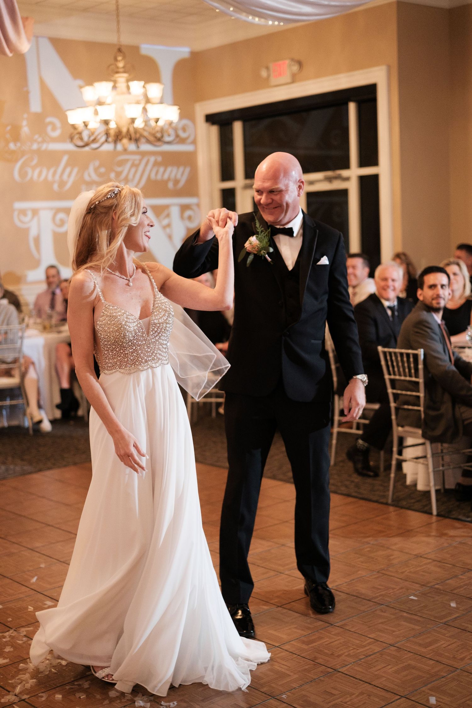 Wedding guests dance and celebrate together on a warm-lit ballroom dance floor during an evening reception.