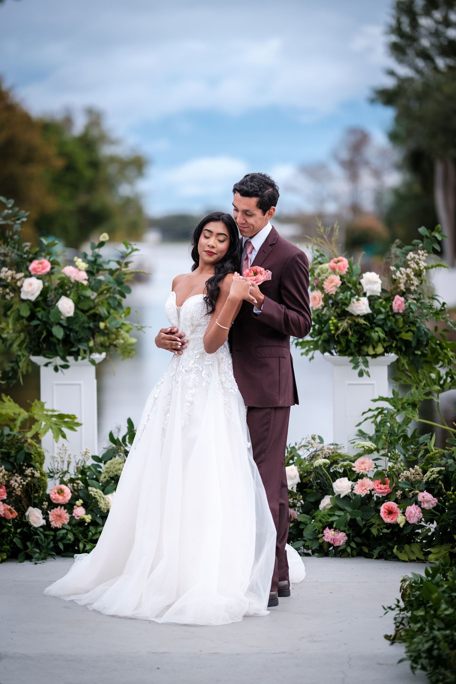 A couple shares a romantic moment on their wedding day surrounded by blooming pink and white roses in a garden setting.