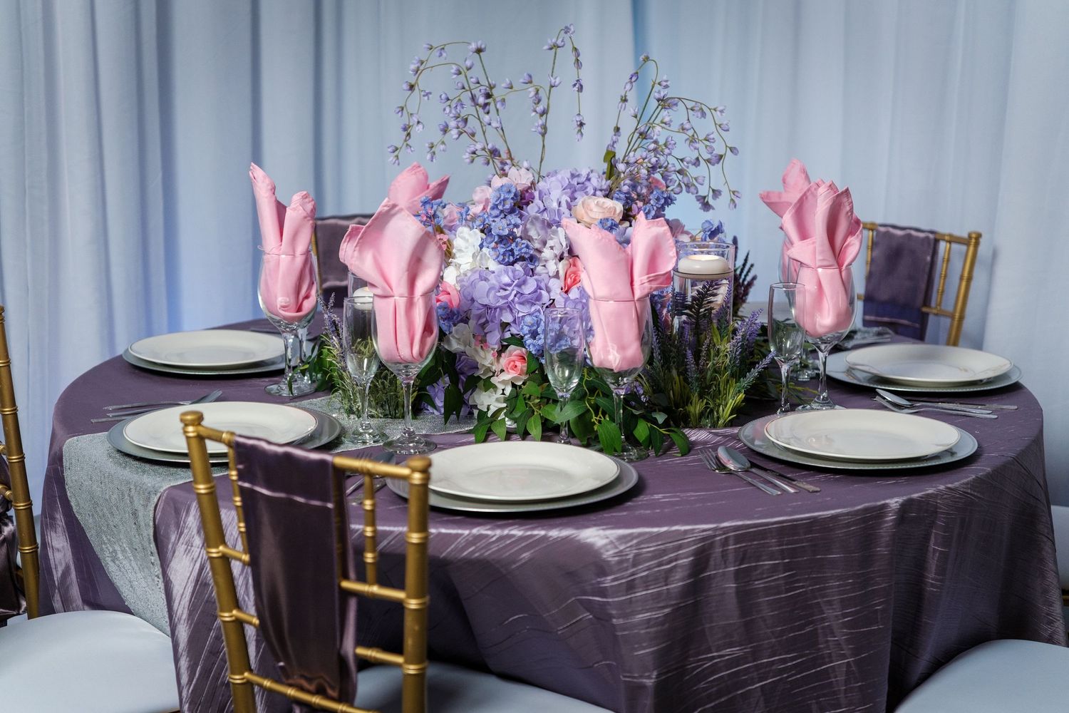 Elegant table setting with pink tulips and purple flowers on a plum-colored tablecloth with gold chiavari chairs.