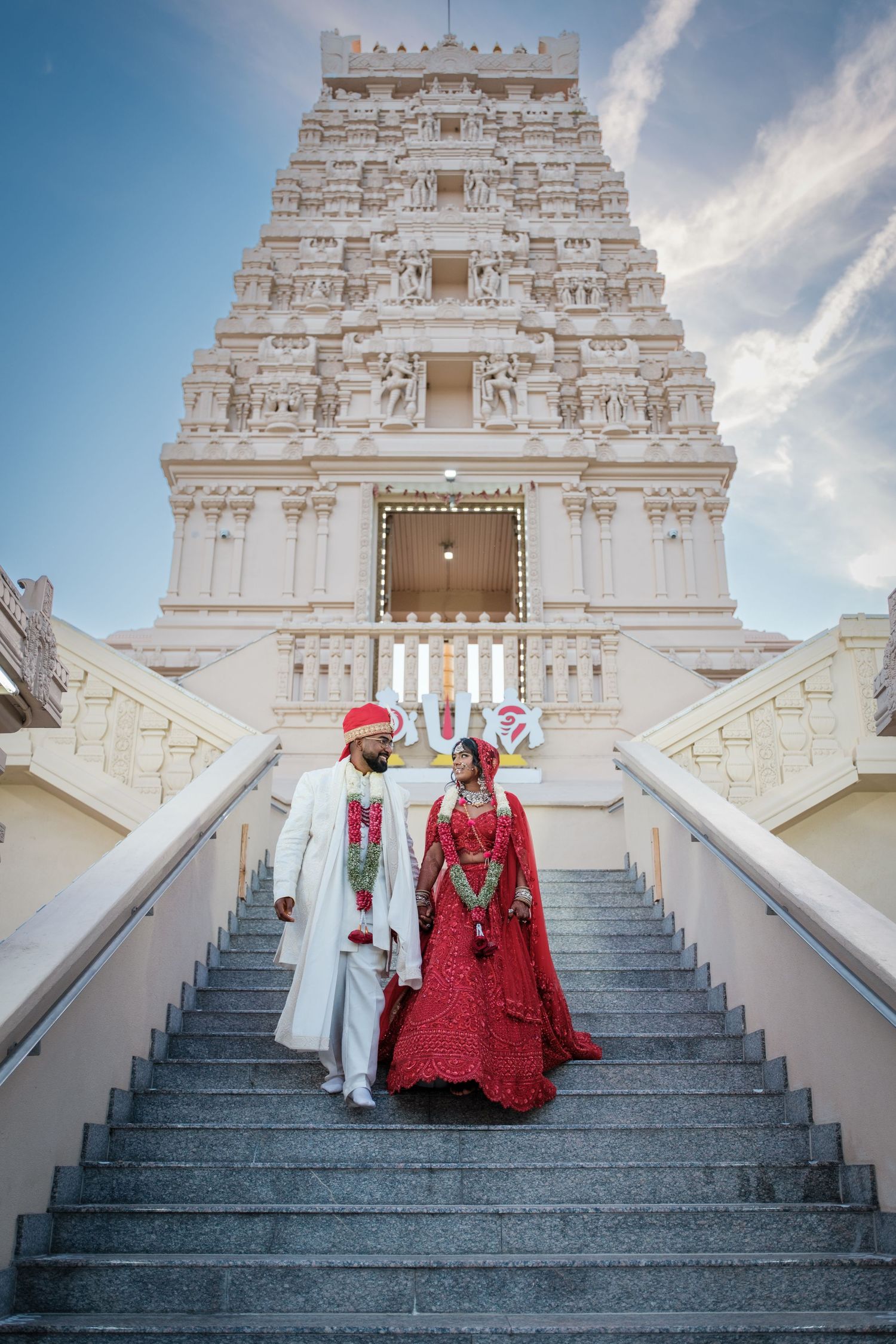 Indian bride and groom in traditional attire descending temple stairs during Hindu wedding ceremony.