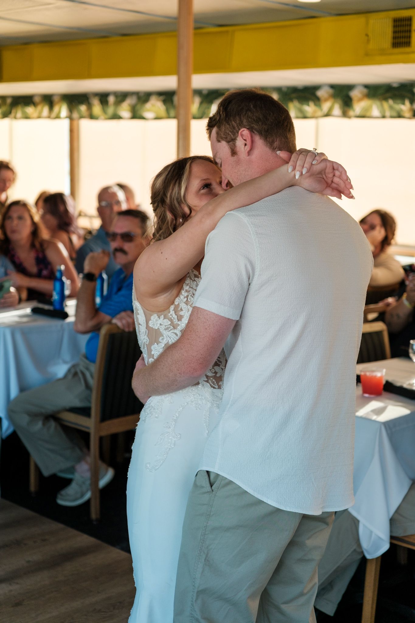A couple shares their first dance at a wedding reception while guests watch from tables with white linens.