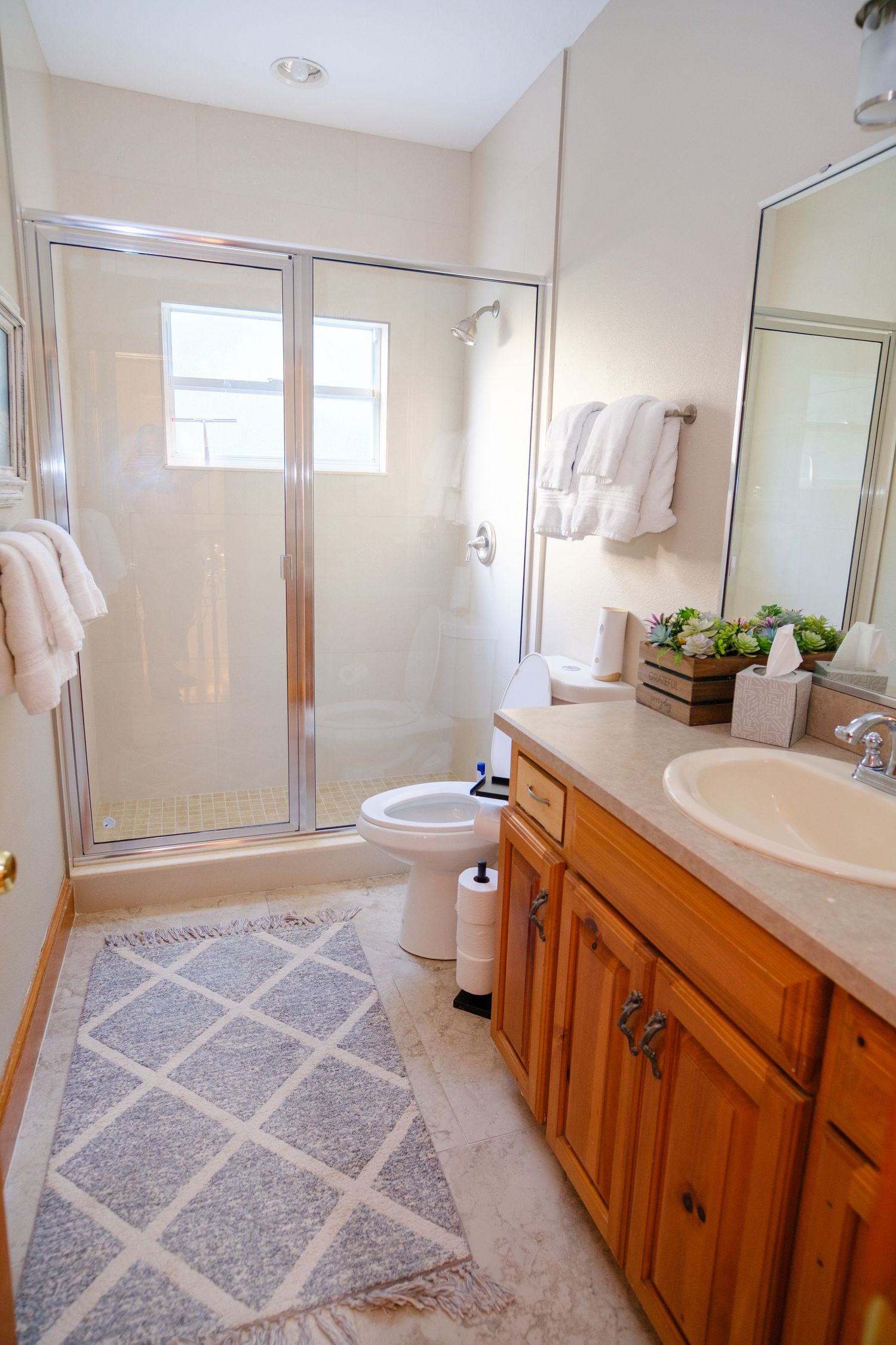Modern bathroom interior with glass shower door, wooden vanity cabinet, white towels and geometric pattern bathroom rug.
