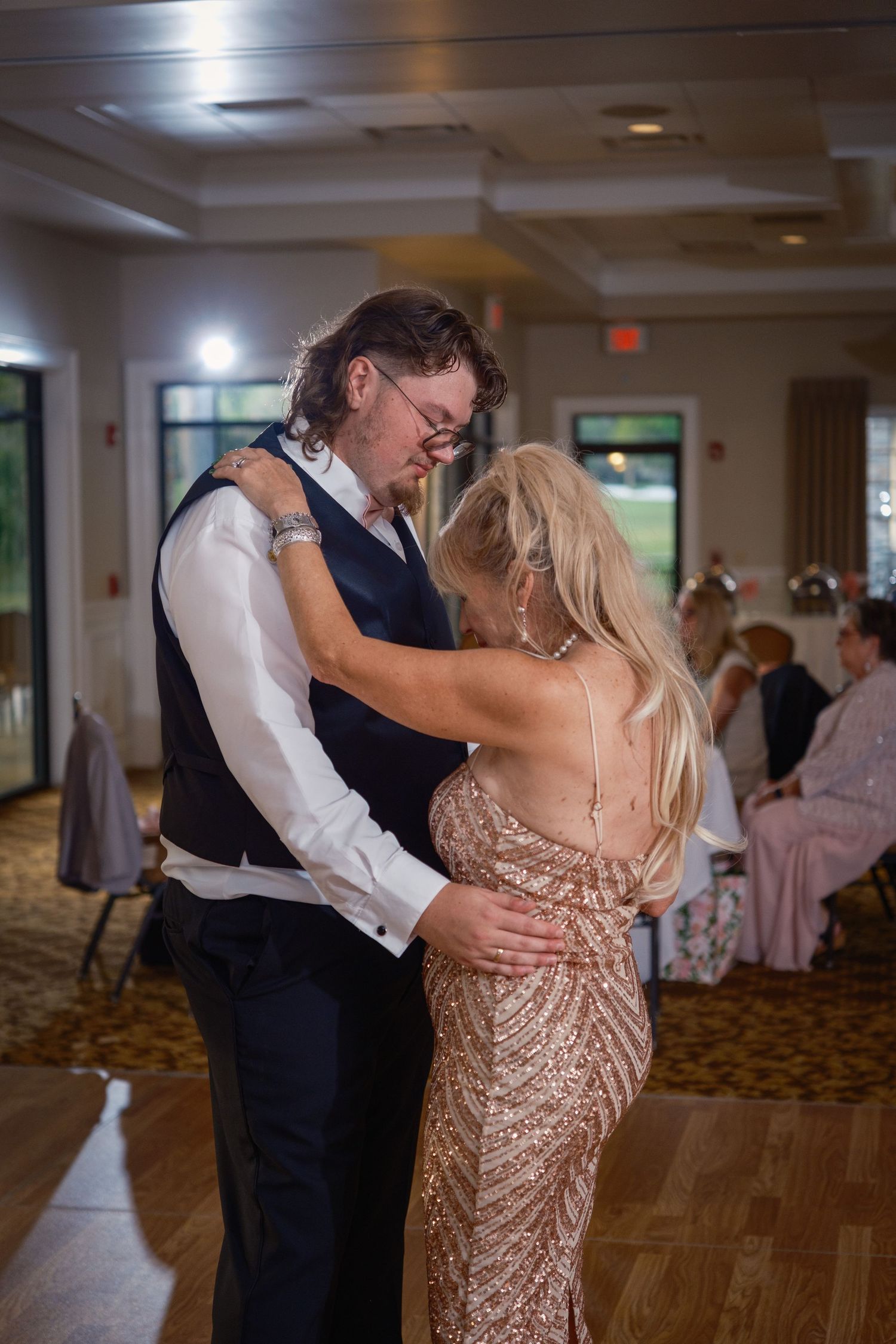Groom dances with woman in gold sequin dress at wedding reception celebration.
