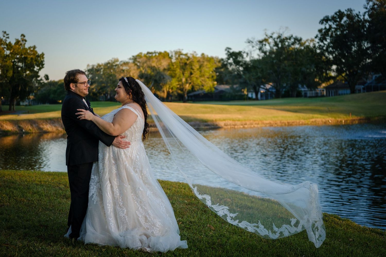 A romantic sunset wedding photoshoot by a serene lake with a long flowing veil catching the golden light.