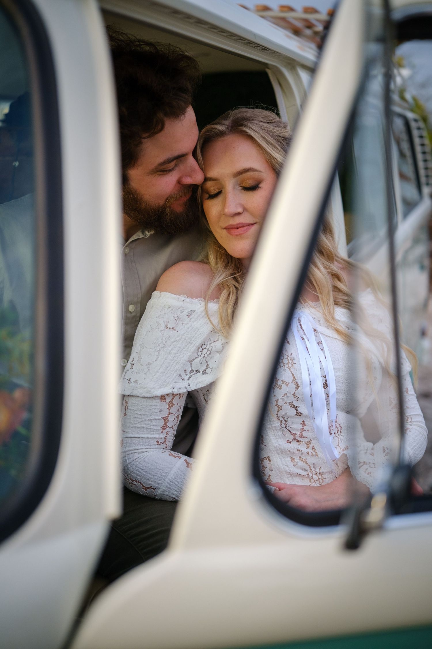 A romantic couple shares an intimate moment inside a vintage car viewed through the window frame.