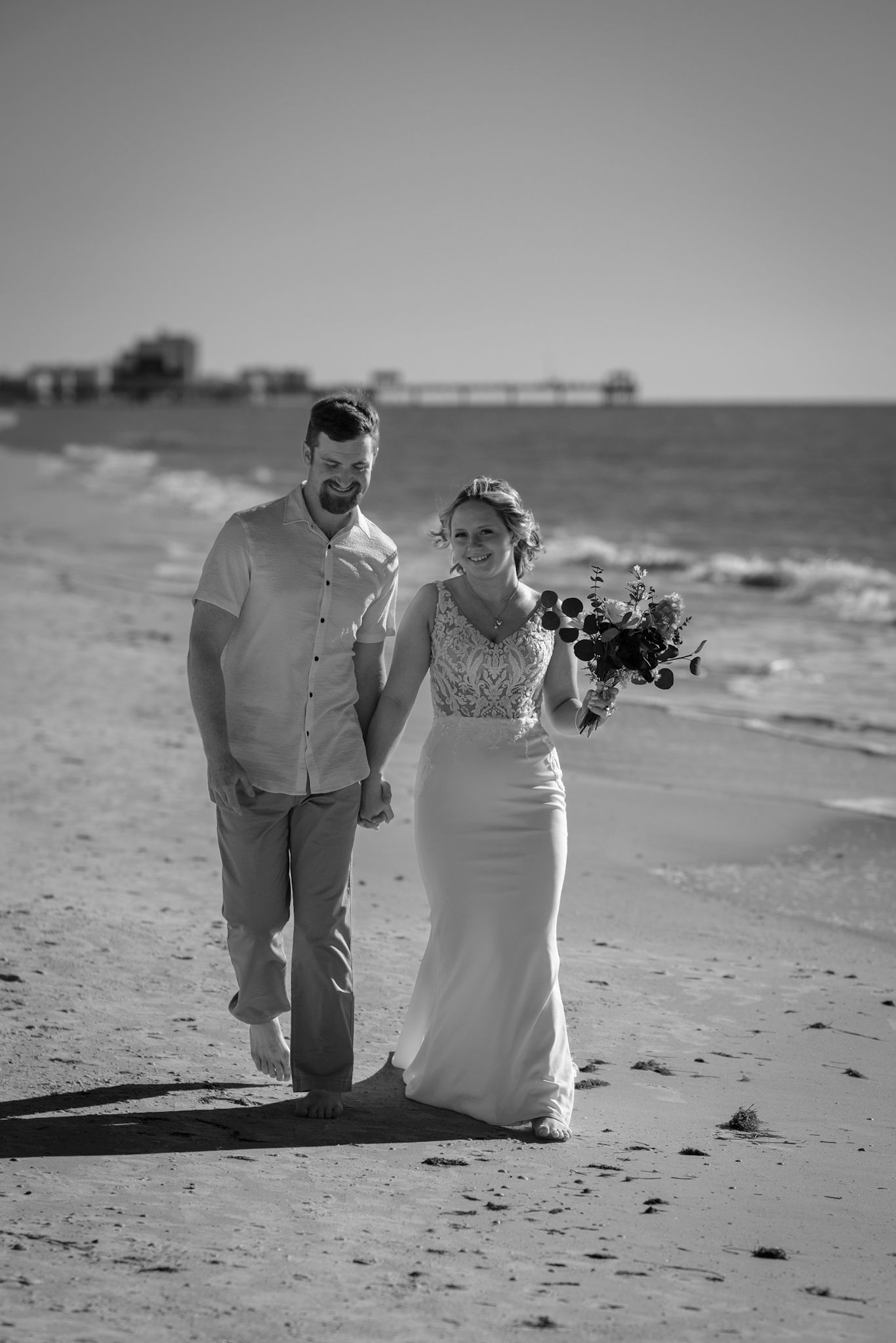 Black and white beach wedding photos showing couple sitting together on sandy shore with ocean waves in background.