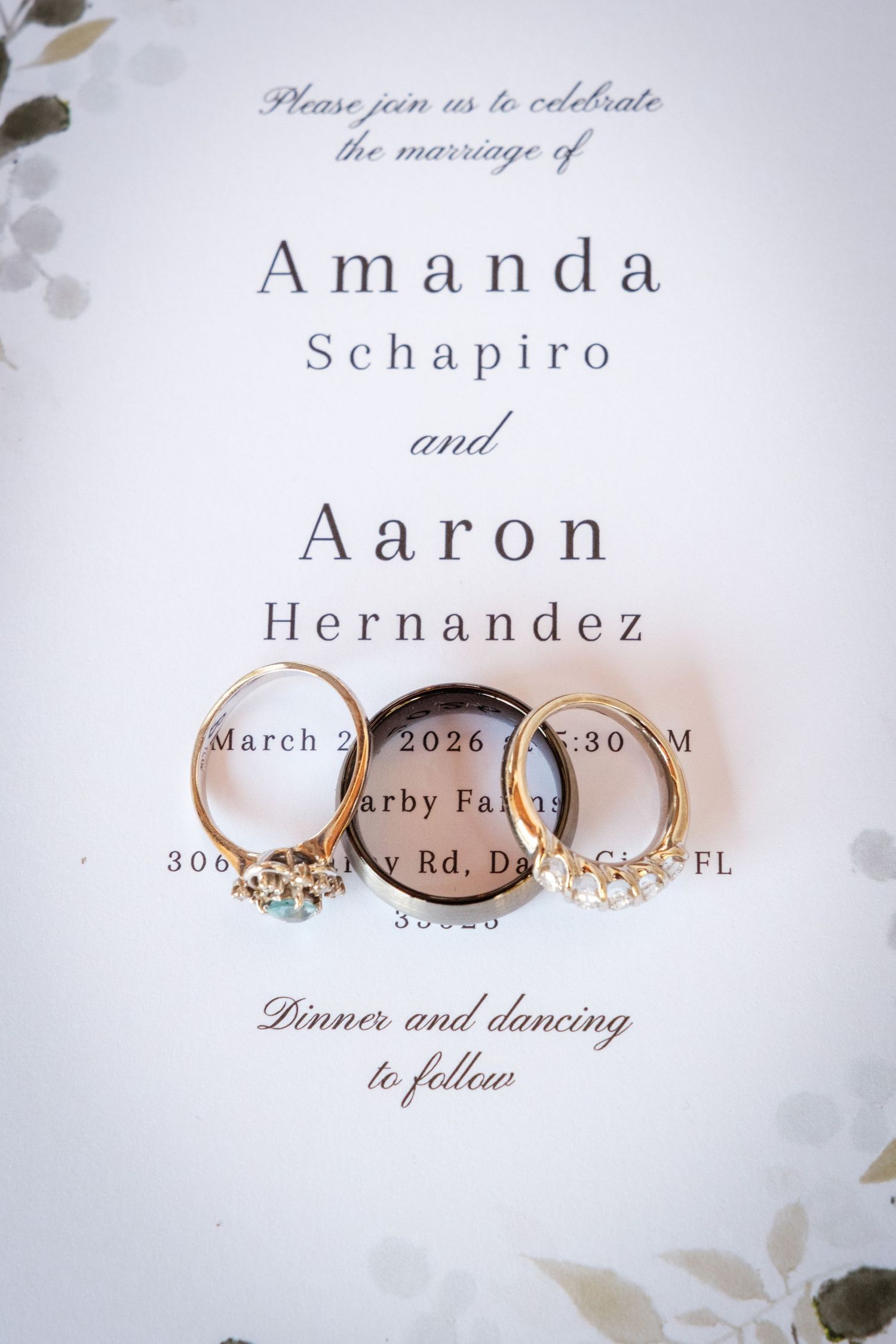Wedding invitation for Amanda Schapiro and Aaron Hernandez with gold rings resting on white card.