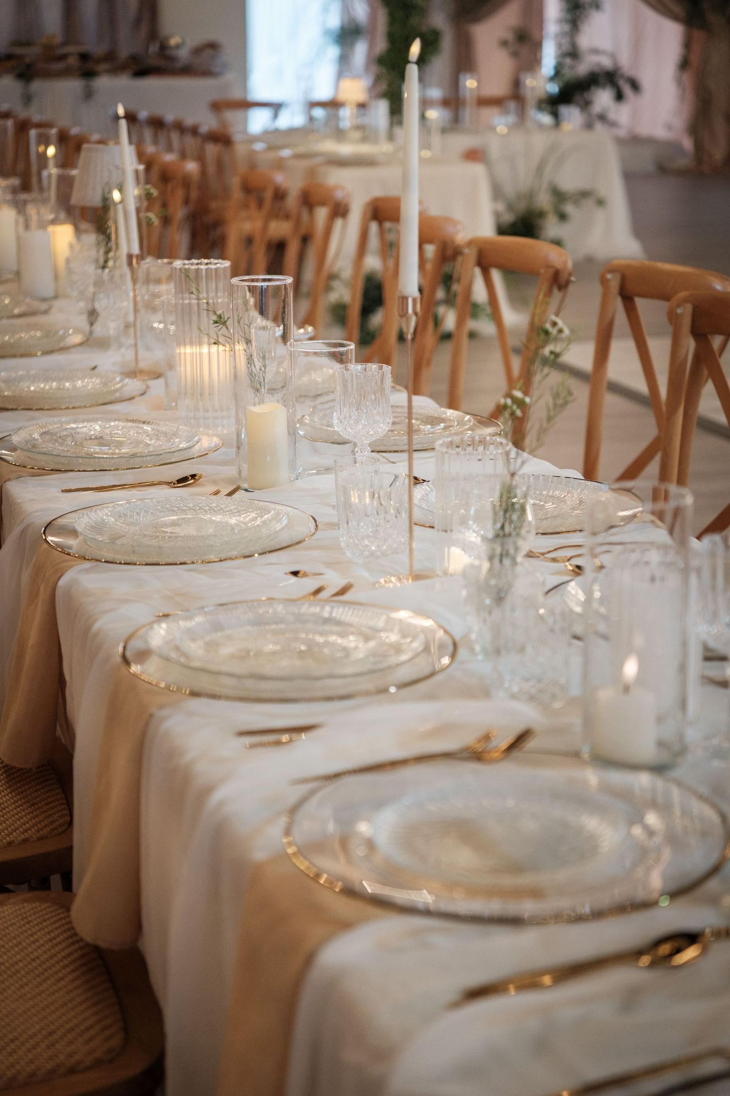 Elegant wedding reception table set with white linens, crystal glassware, gold accents, and candles on a long dining table.