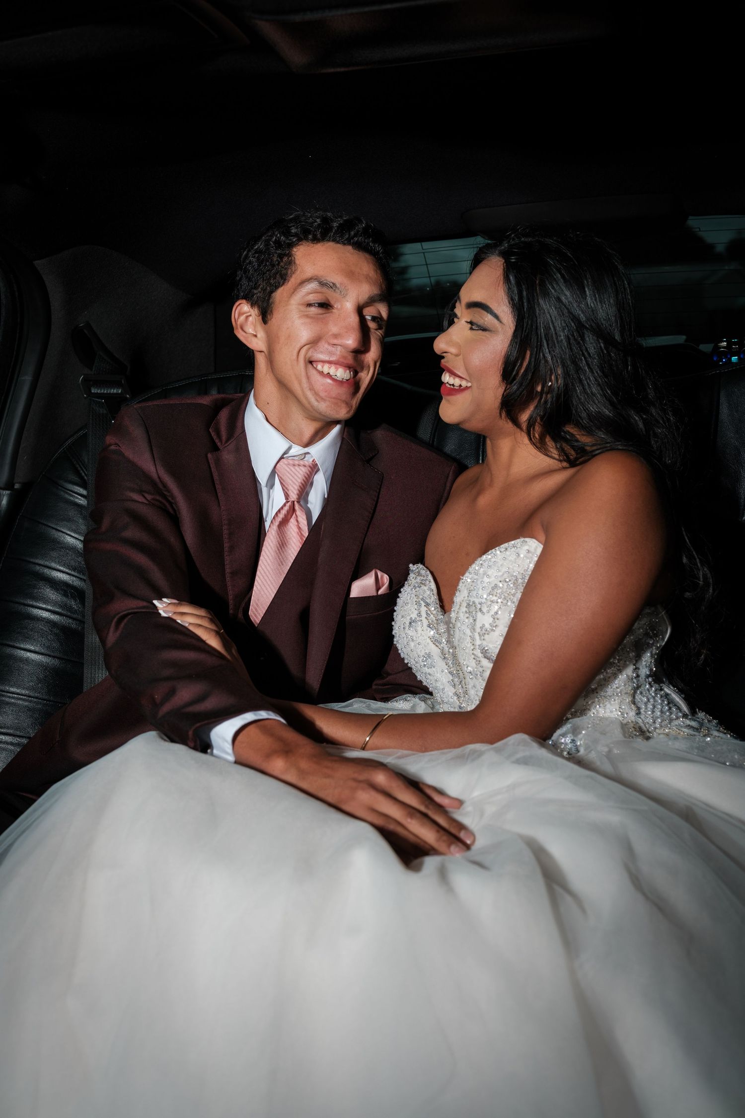 Newlyweds share tender moments together in the back of a luxury car, displaying their joy and affection.