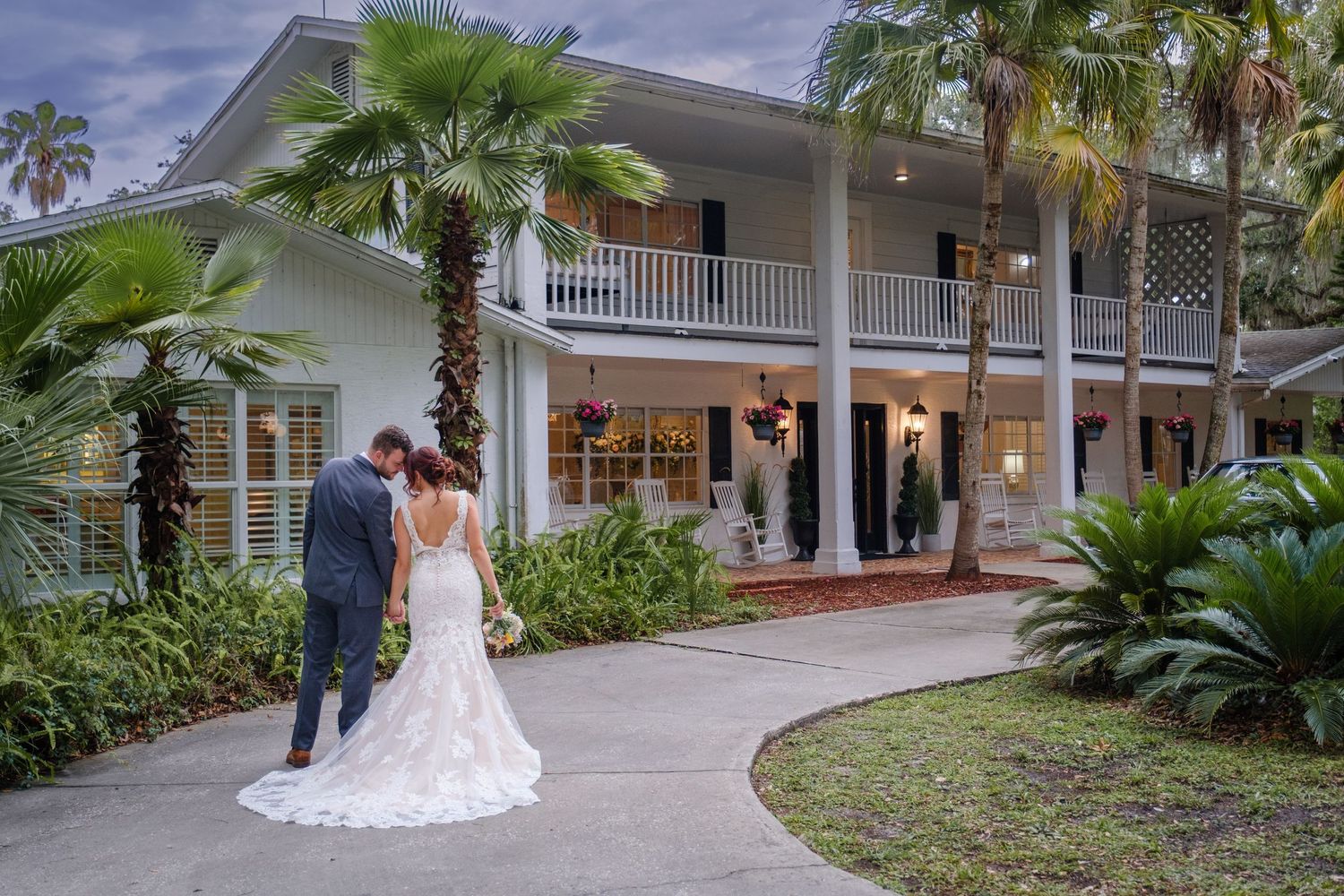 A beautiful white wedding dress flows elegantly against a backdrop of palm trees and a coastal style home.