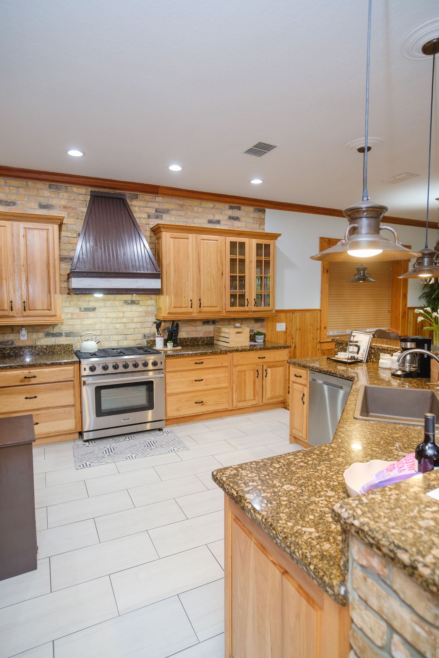 Modern kitchen with light wood cabinets, granite countertops, stone backsplash, and stainless steel appliances.