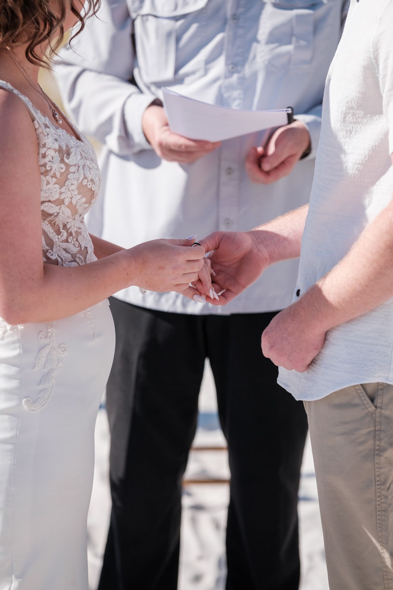Wedding guests in white attire gathered for an outdoor beach ceremony under clear blue skies.