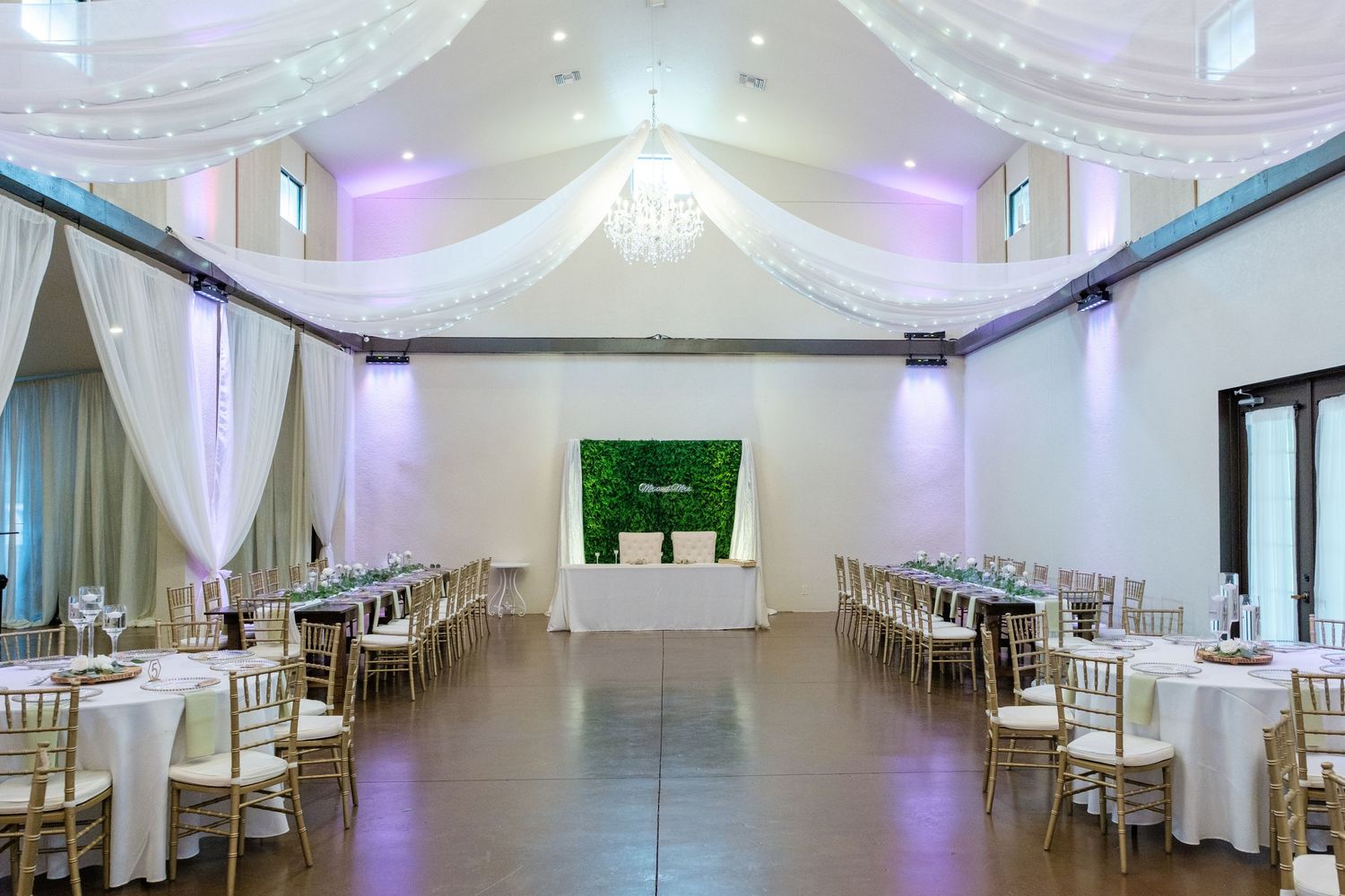 Panoramic view of an elegant white banquet hall with purple accent lighting and tables set for a formal event.