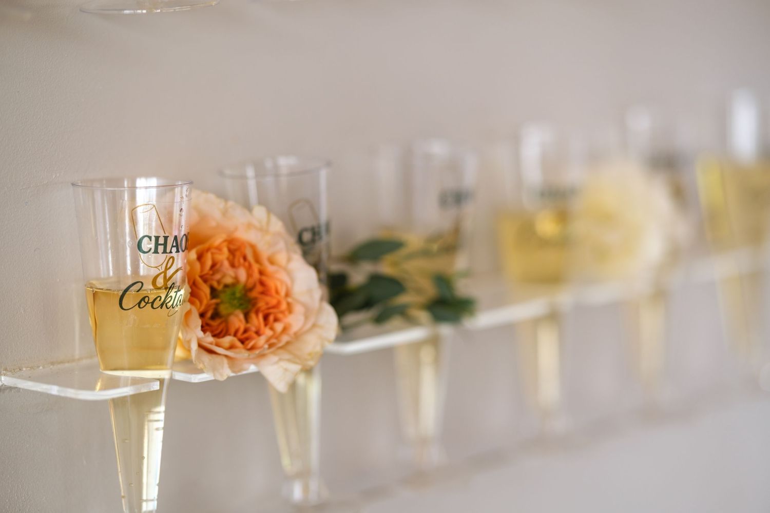Champagne glasses lined up with a delicate peach rose resting against one glass filled with golden bubbly.