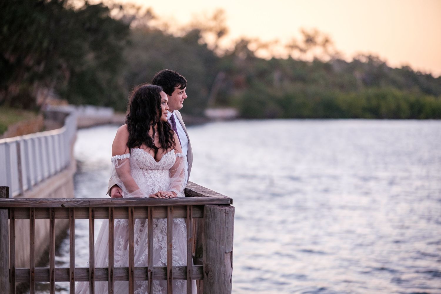 A romantic couple sits together on a wooden dock overlooking a serene lake at sunset.
