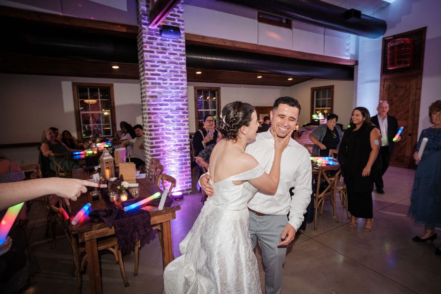 Bride and groom dancing surrounded by guests with colorful glow sticks at wedding reception.