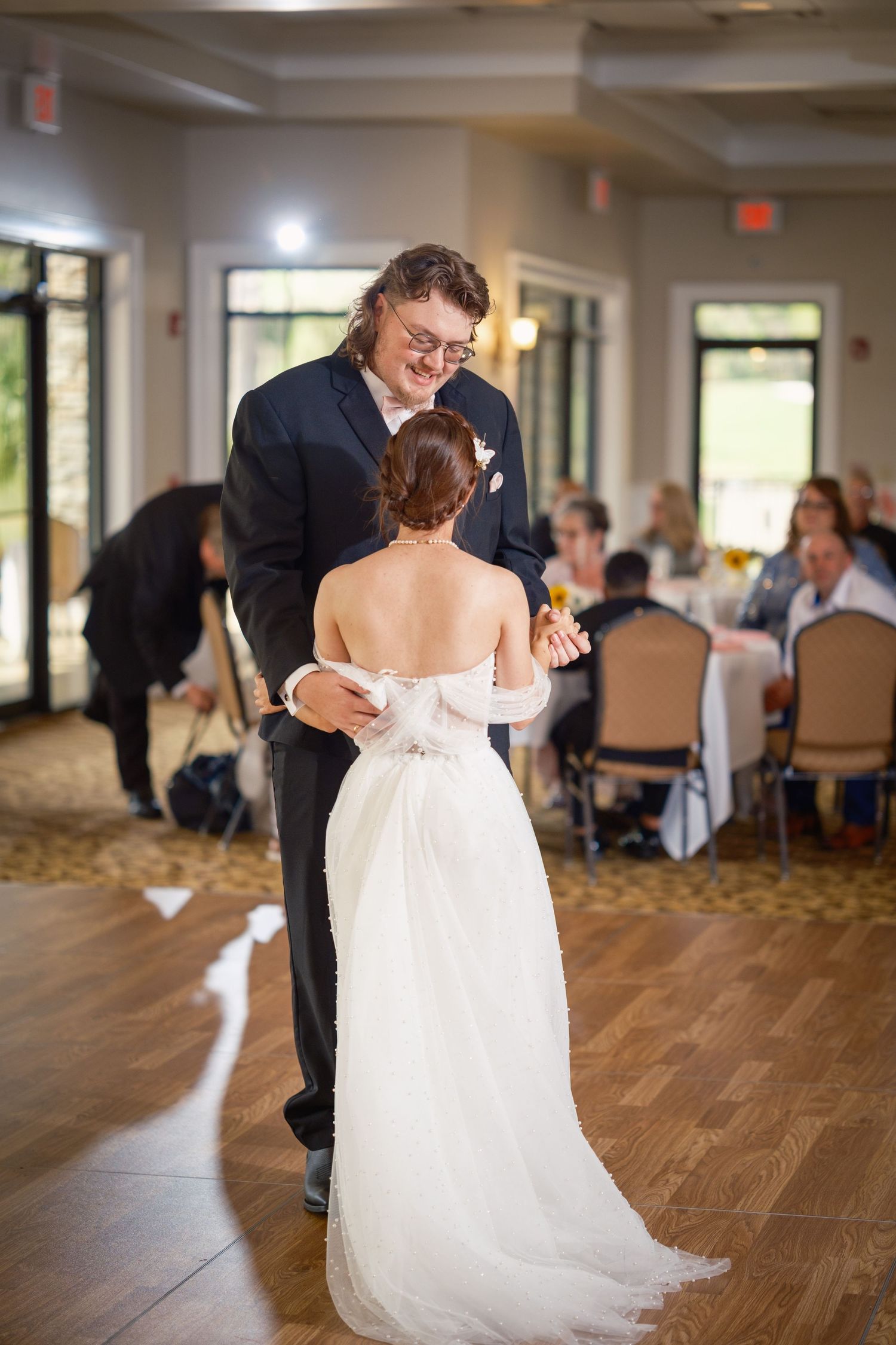 Bride and groom share their first dance at wedding reception, bride in elegant backless white gown.