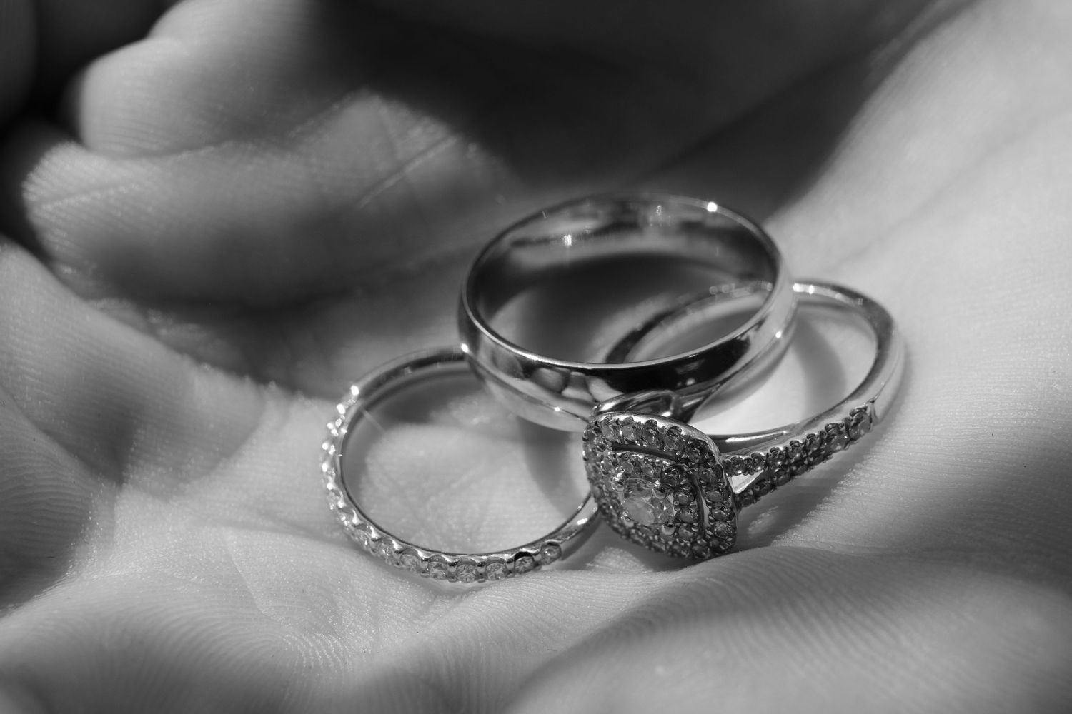 Three elegant wedding rings with diamond details rest in a palm, captured in black and white photography.